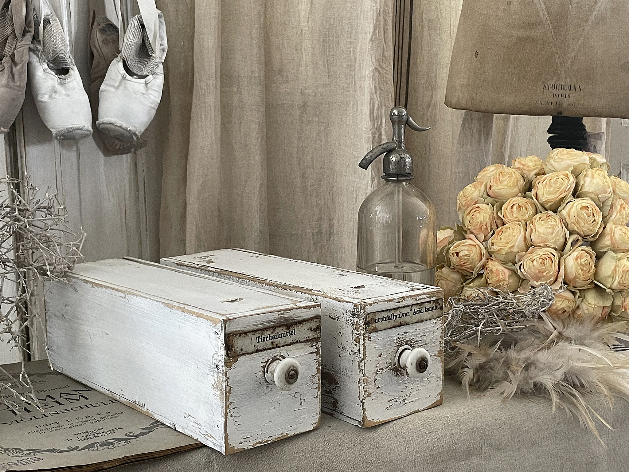 Zwei weiße Holzschatullen mit Knöpfen, umgeben von einer Glasflasche und einem Blumenstrauß.