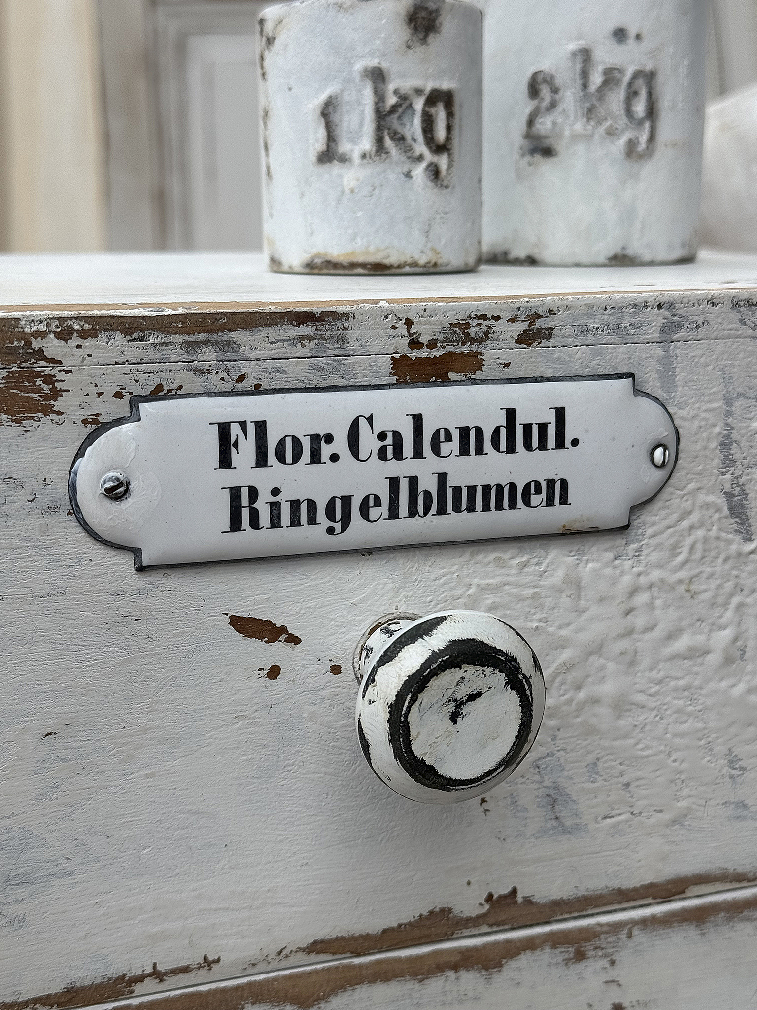 Blick auf ein Holzregal mit Beschriftung für Ringelblumen Holzregal mit der Beschriftung „Flor: Calendul. Ringelblumen“ und Gewichtsanzeigen der Behälter
