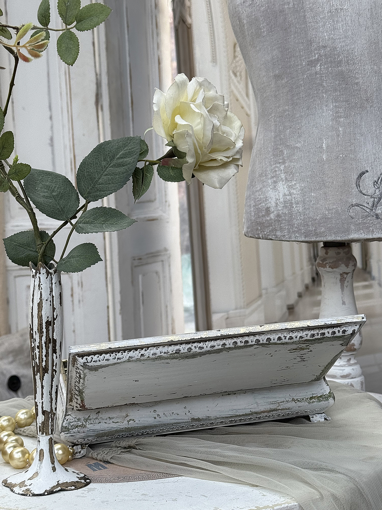 Deko-Arrangement mit Keramikvase, Rosenblüte und eleganter Tischdecke Dekorativer Tisch mit einer weißen Keramikvase, einer Rose und einem antiken Tablett