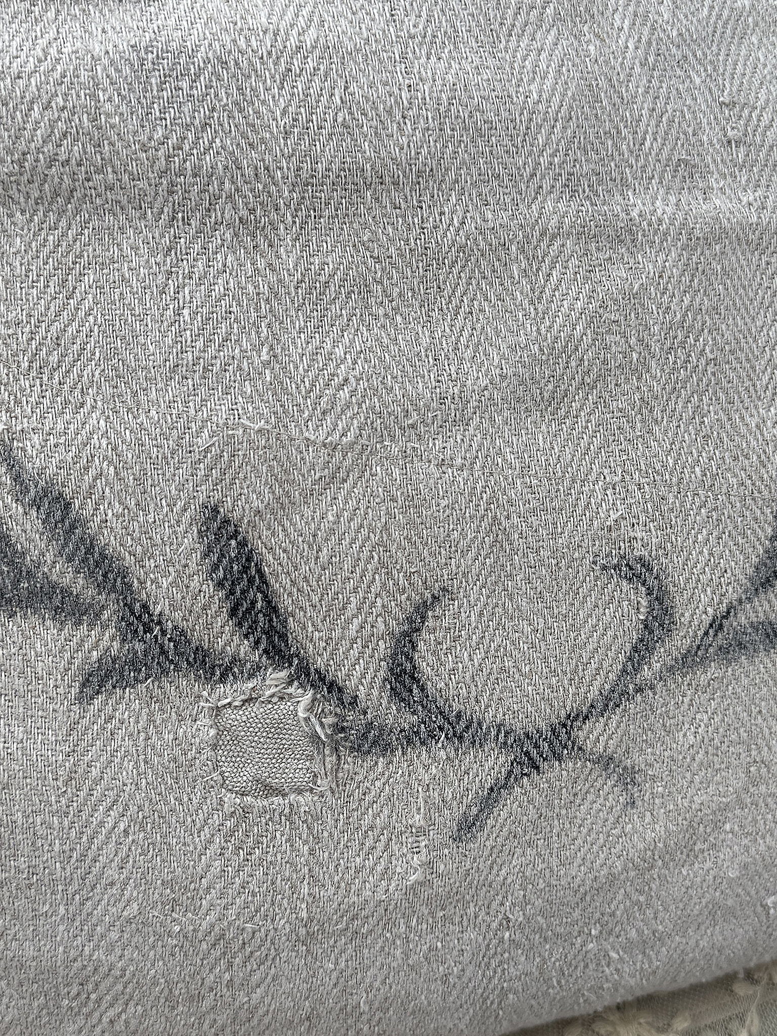 Nahaufnahme eines grauen Stoffes mit dezentem Muster und kleinen Beschädigungen. Detailaufnahme eines grauen Materials mit einem Muster und einer kleinen Einschneidung.
