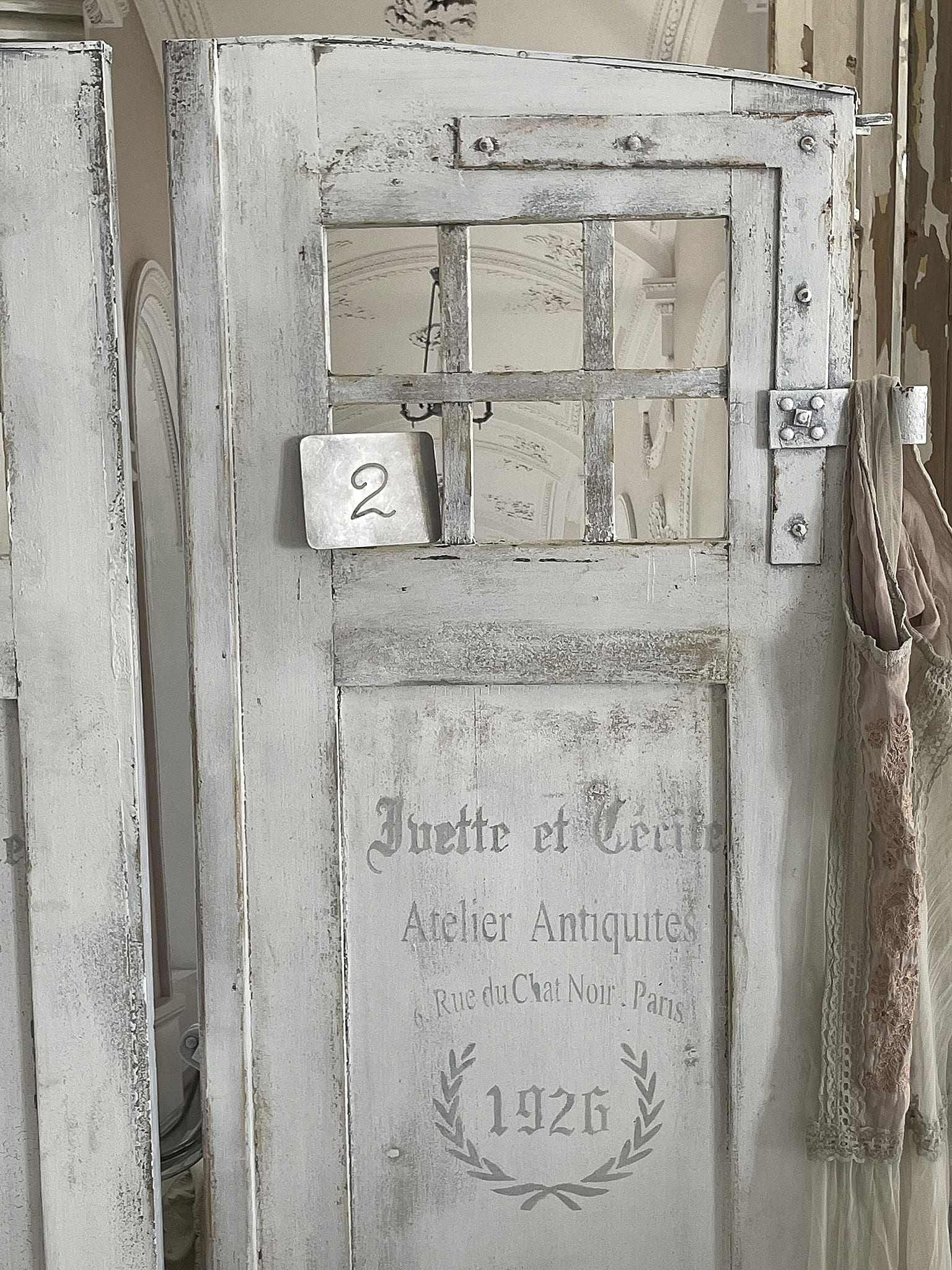 Detailaufnahme einer antiken weißen Tür mit der Nummer 2 und dem Schriftzug 'Jevette et Cerise, Atelier Antiquites, 1926'.