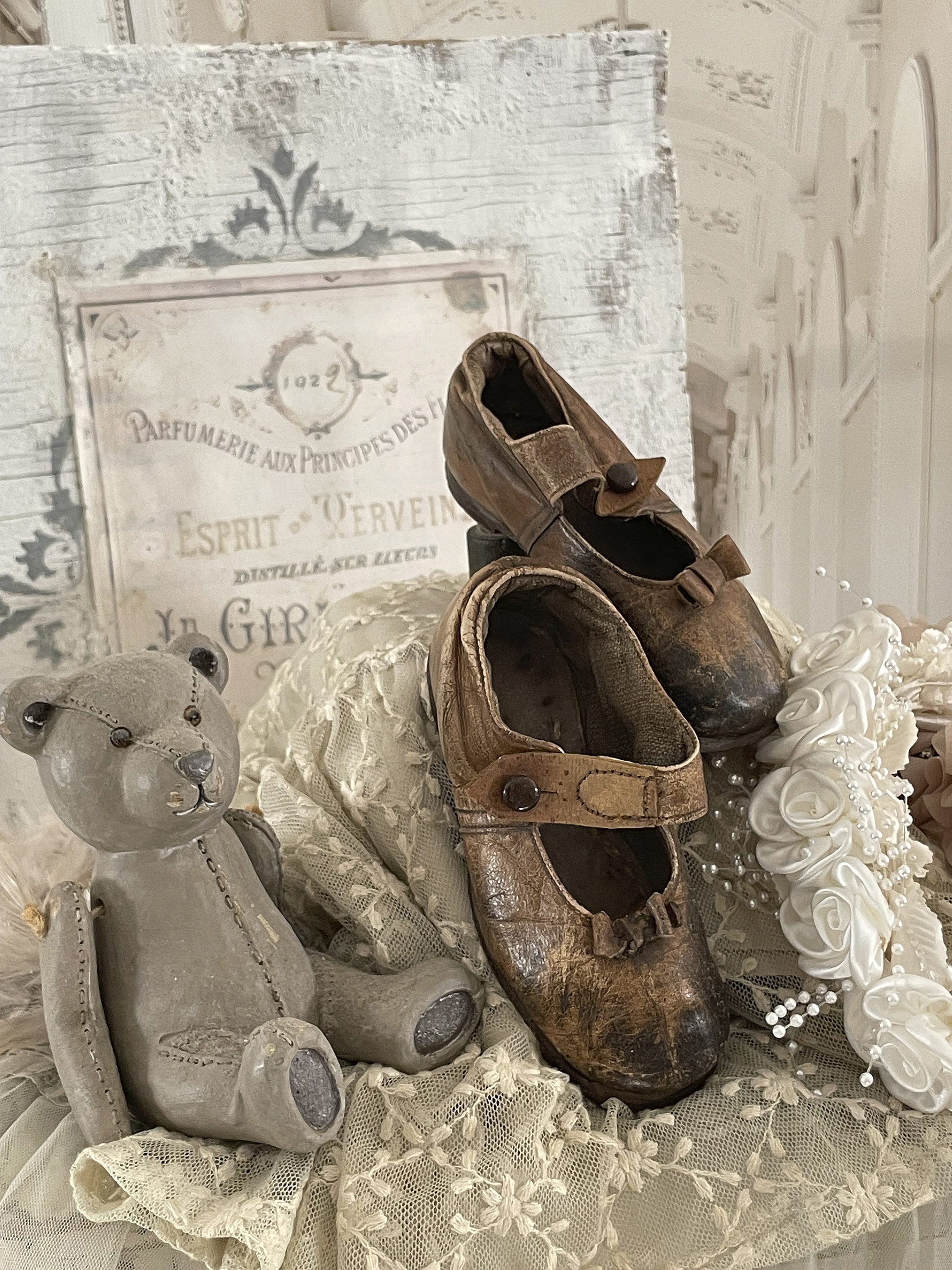 Nostalgisches Arrangement mit antiken Kinderschuhen, einem grauen Teddy und romantischem Stoff
