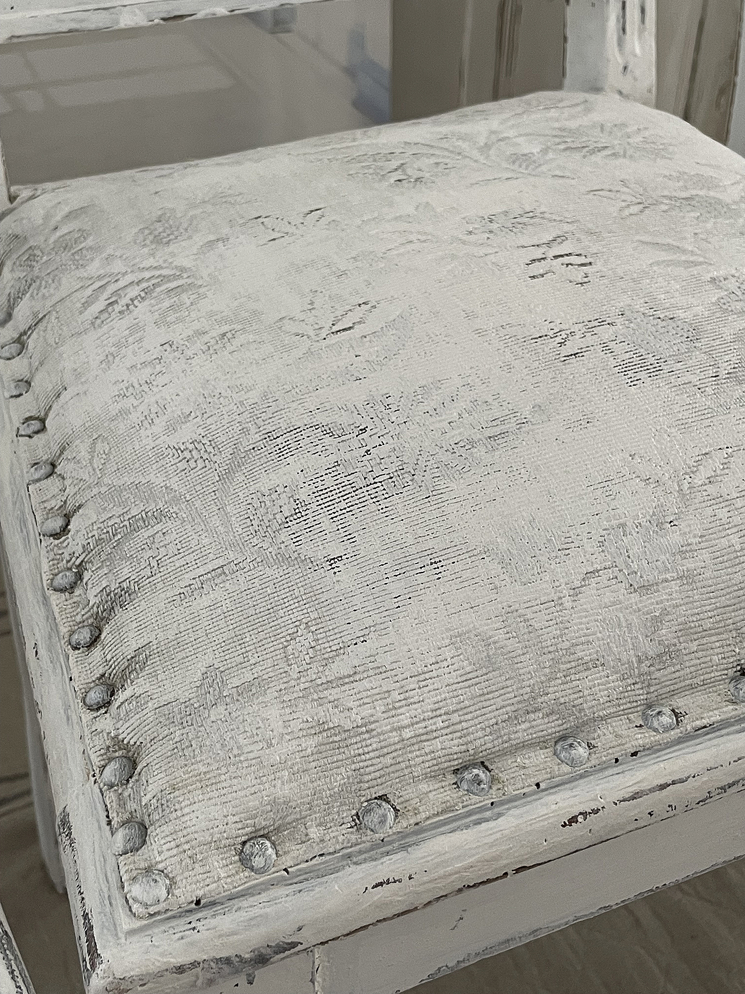 Eleganter Stuhl mit filigranem, gestepptem Sitzpolster in Weiß Detailaufnahme eines eleganten Stuhls mit einem weißen, gesteppten Sitzpolster und dekorativen Nägeln.