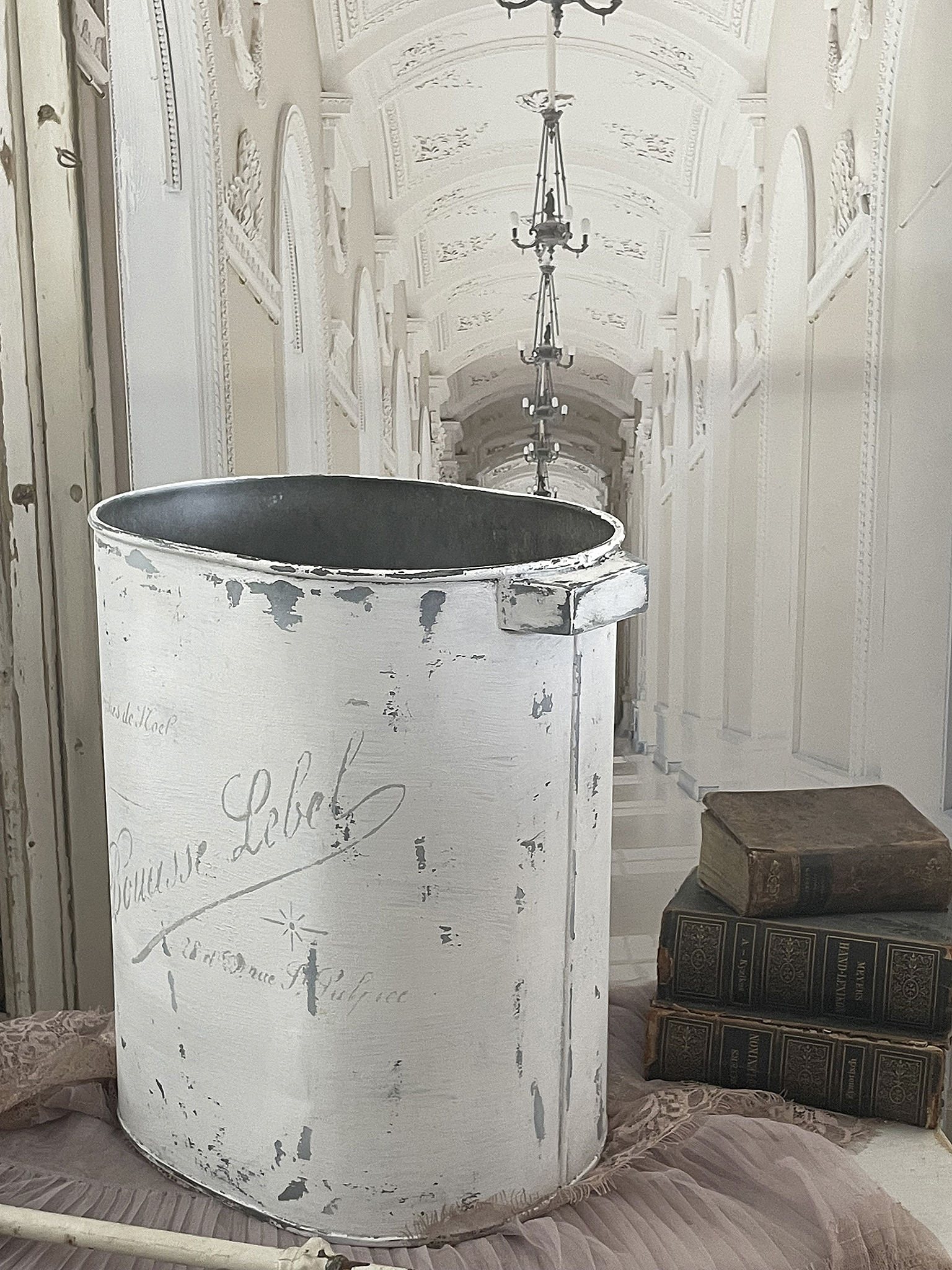 Vintage Aufbewahrungseimer mit Beschriftung und alten Büchern Ein weißer vintage Aufbewahrungseimer steht neben alten Bücherstapeln in einem eleganten Raum.