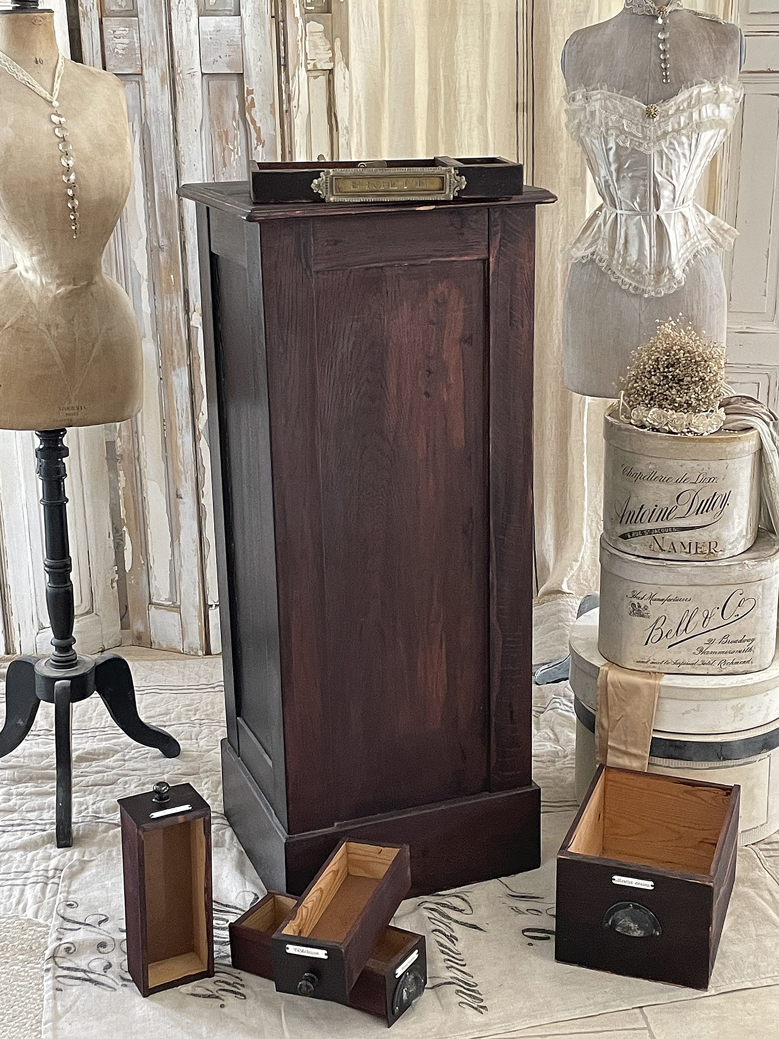 Vintage Holzschrank mit offenen Schubladen und Schneiderpuppen im Hintergrund