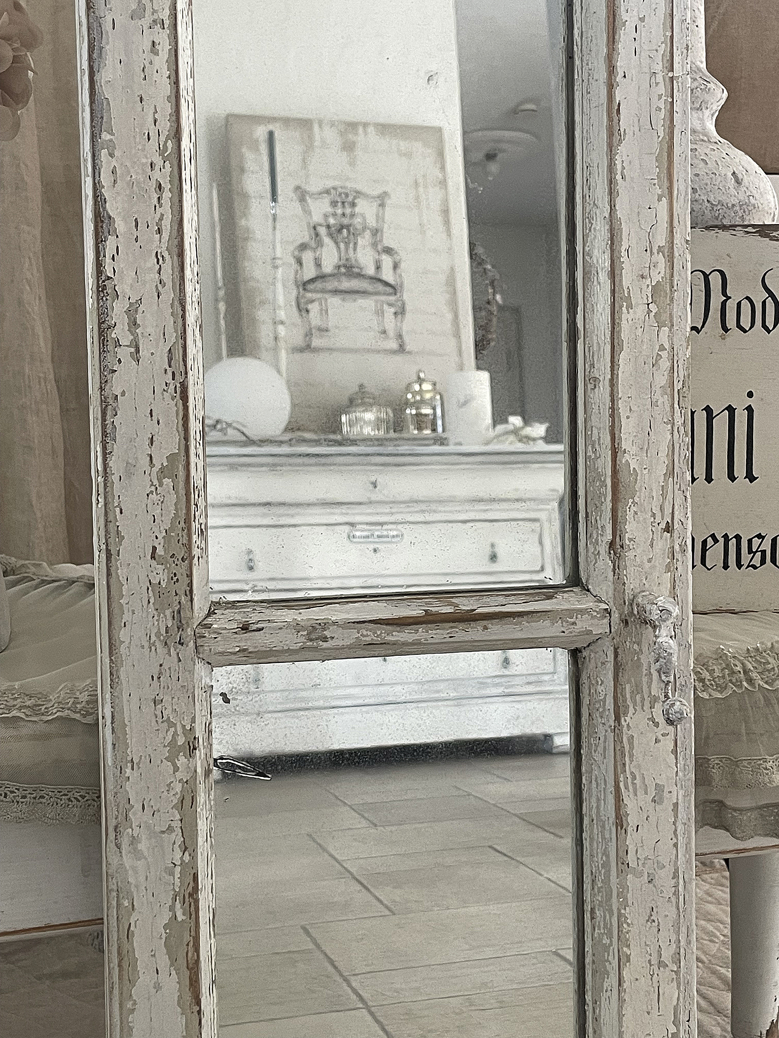 Vintage Spiegel mit shabby-chic Rahmen in heller Wohnumgebung Ein Vintage-Spiegel mit einem abgenutzten Rahmen in einem hellen Raum, reflektiert ein Möbelstück und eine Kunstzeichnung.
