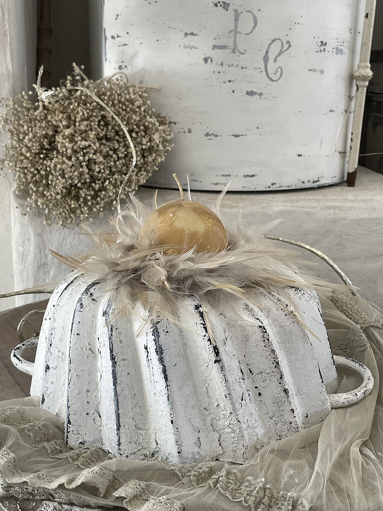 Dekorative Backform mit Federn und goldener Kugel Helle Backform dekoriert mit Federn und einer goldenen Kugel auf einem zarten Stoff