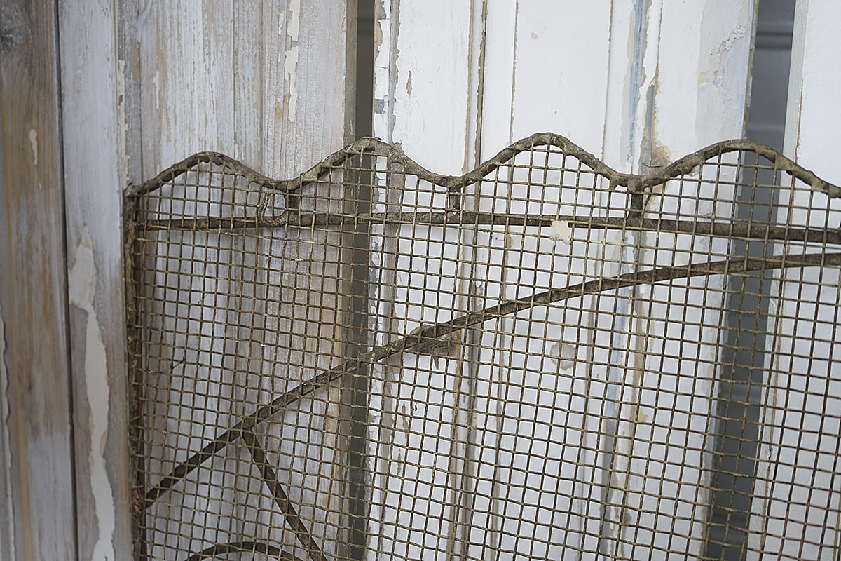 Detaillierte Ansicht einer rustikalen Metallgittertür, die aus alten Holzpanelen besteht, mit sichtbarem Farbabrieb.