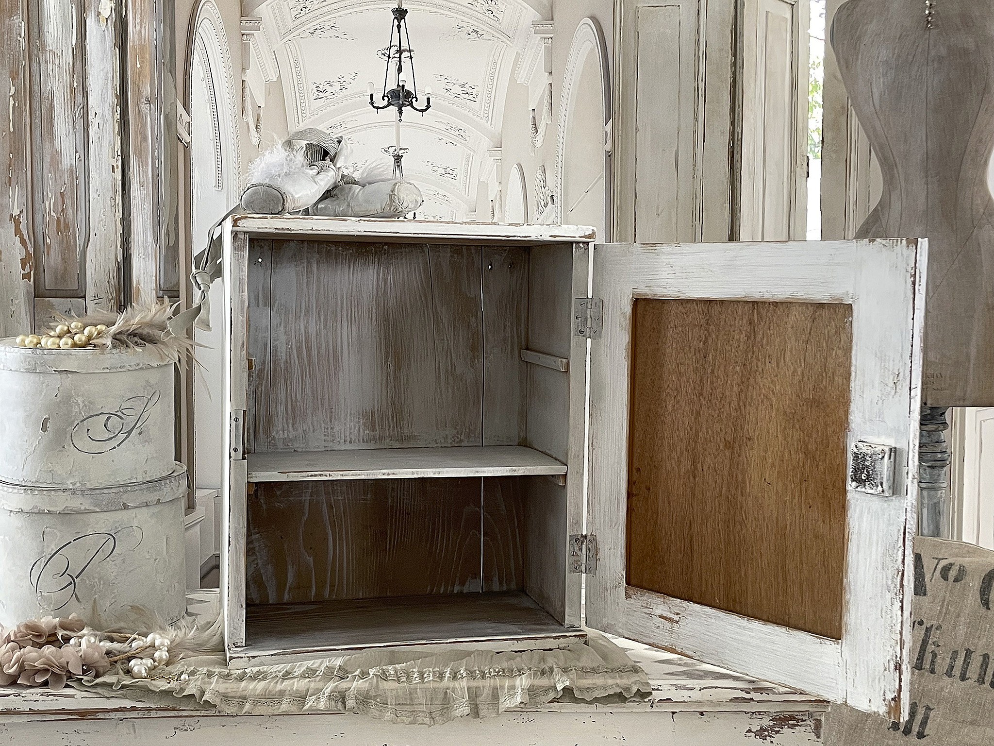 Vintage Holzschrank mit weißer Lackierung und offenem Türdesign Offener Vintage Holzschrank in Weiß, dekoriert mit nostalgischen Accessoires