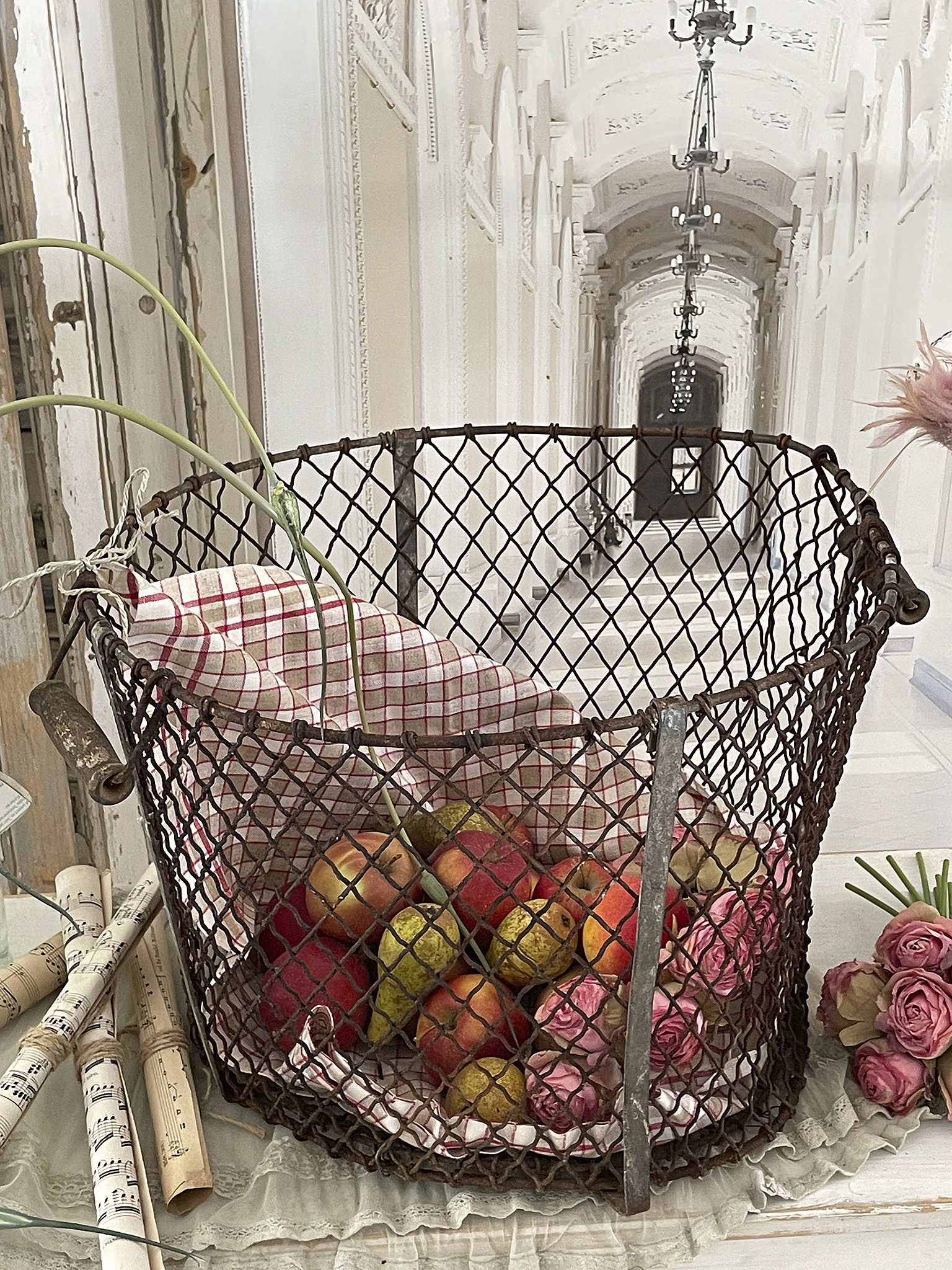 Rustikaler Gitterkorb mit Äpfeln, Birnen und Rosen in historischem Ambiente. Ein Gitterkorb mit frischen Früchten und Rosen auf einem eleganten Tisch in einem klassischen Innenraum.
