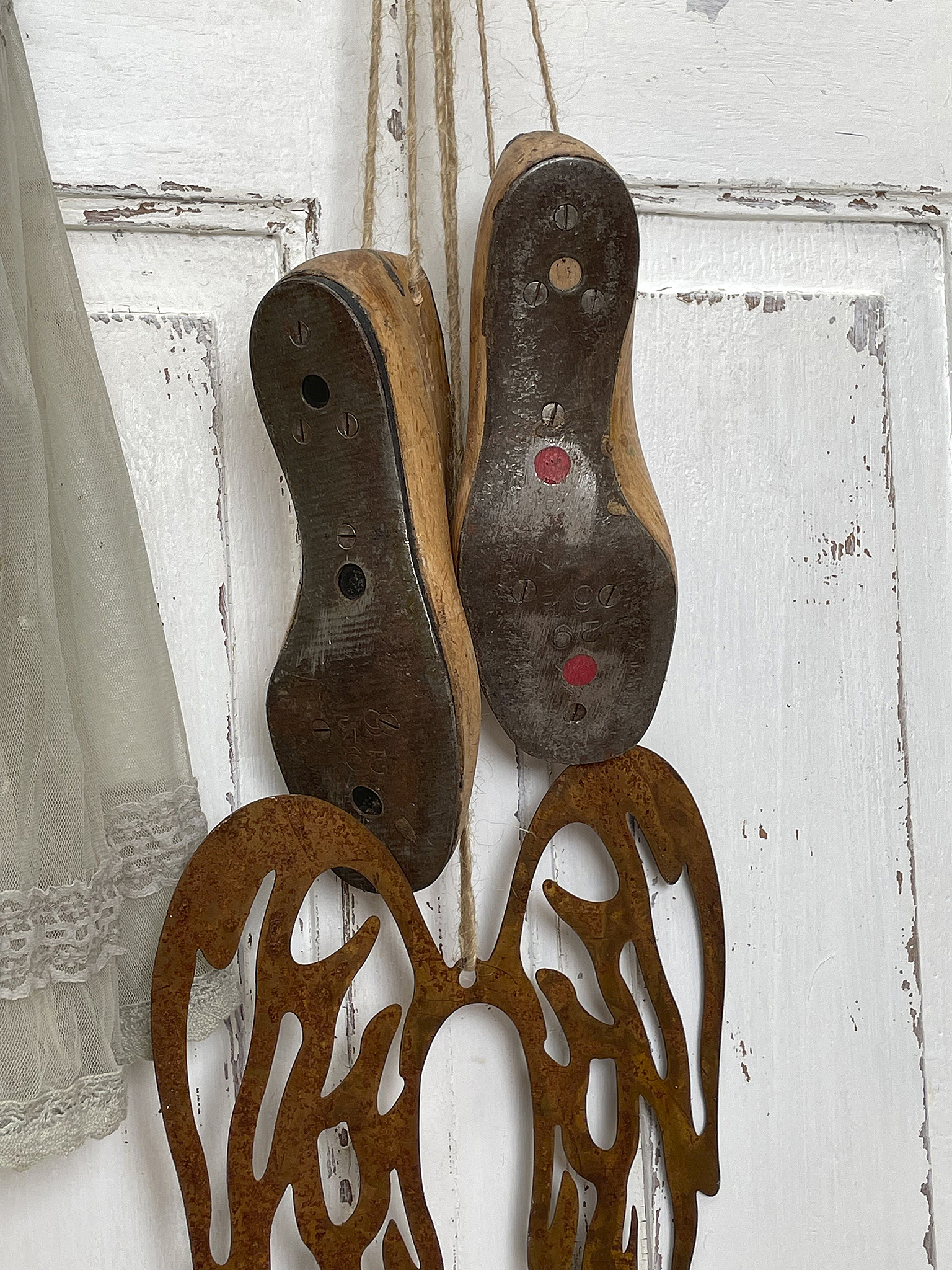 Holzschuhe mit abgenutzten Sohlen, hängend an einer Wand, kombiniert mit künstlerischen Metallflügeln.