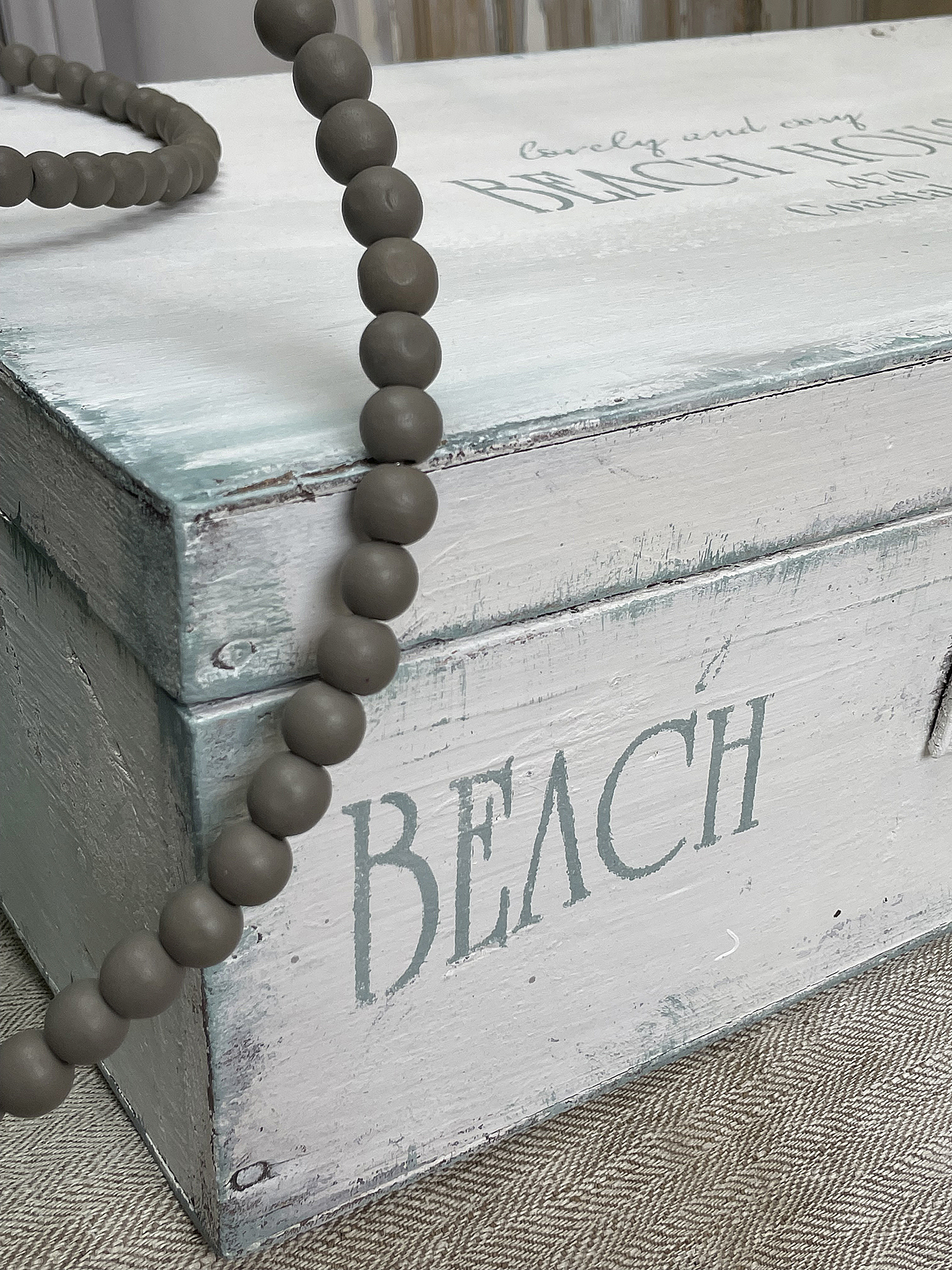 Dekorativer Holzkasten mit Strandmotiv und stylischem Schmuckstück Dekorativer Holzkasten mit der Aufschrift BEACH und einer Perlenkette