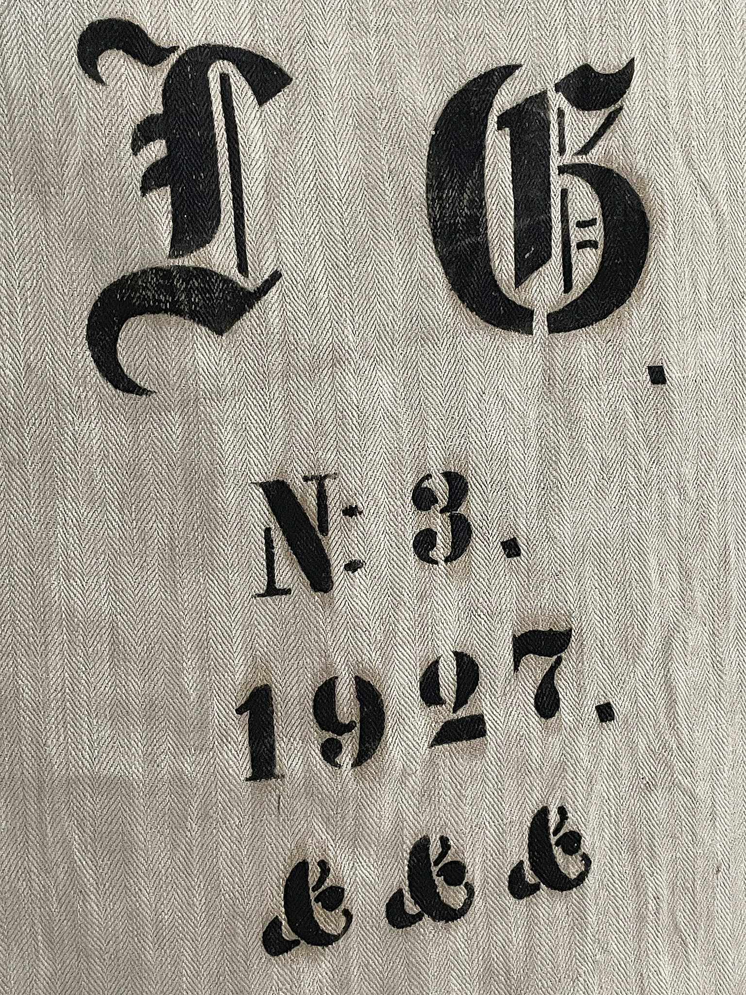 Historische Grafik mit den Zahlen 1927, N. 3 und stilisierten Buchstaben Detailaufnahme eines Textiles mit schwarzen Aufdrucken von 1927, N. 3 und dekorativen Elementen.