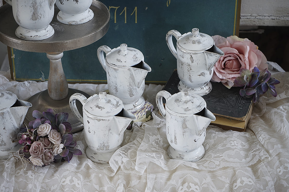 Weißes Kaffeekannen-Set auf einem Tisch mit Blumenarrangement und Buch, dekorativer Hintergrund.