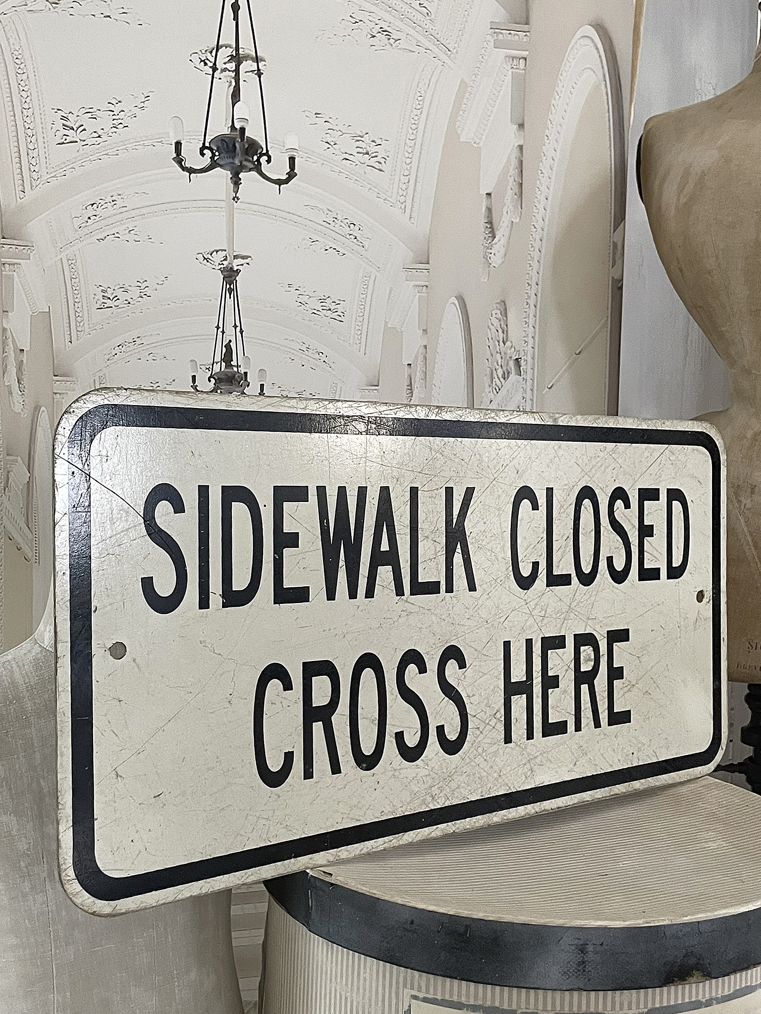 Schild Fußweg gesperrt, hier queren, vor einem Innenraum