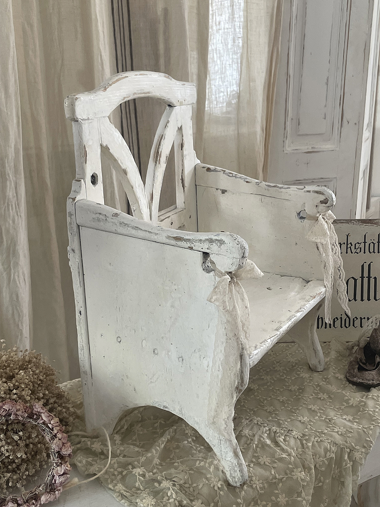 Eleganter vintage Kinderstuhl aus Holz, weiß lackiert, dekoriert mit Bändern, auf einem romantischen Tisch aufgebaut.