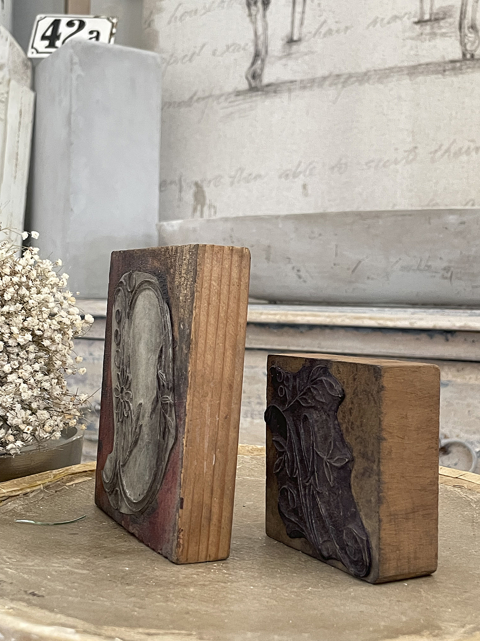 Zwei antike Holzstempel auf einem Holzteller, einer mit Blumenmotiv und der andere mit einem Blattdesign.