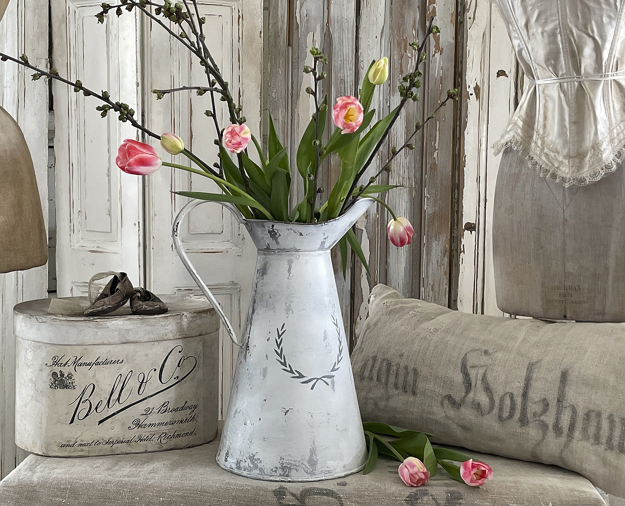 Dekorative Vase mit Tulpen und Ästen für ein stilvolles Zuhause Vase mit bunten Tulpen und Ästen auf einem Tisch, umgeben von vintage Deko und einer Kissen