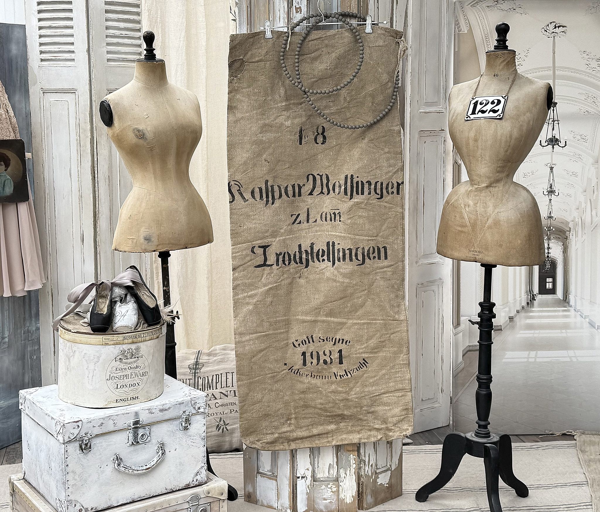 Antike Schneiderpuppen mit Vintage-Accessoires für stilvolle Innendekoration Schneiderpuppen aus Holz neben einer historischen Stoffrolle und einem Aufbewahrungskoffer