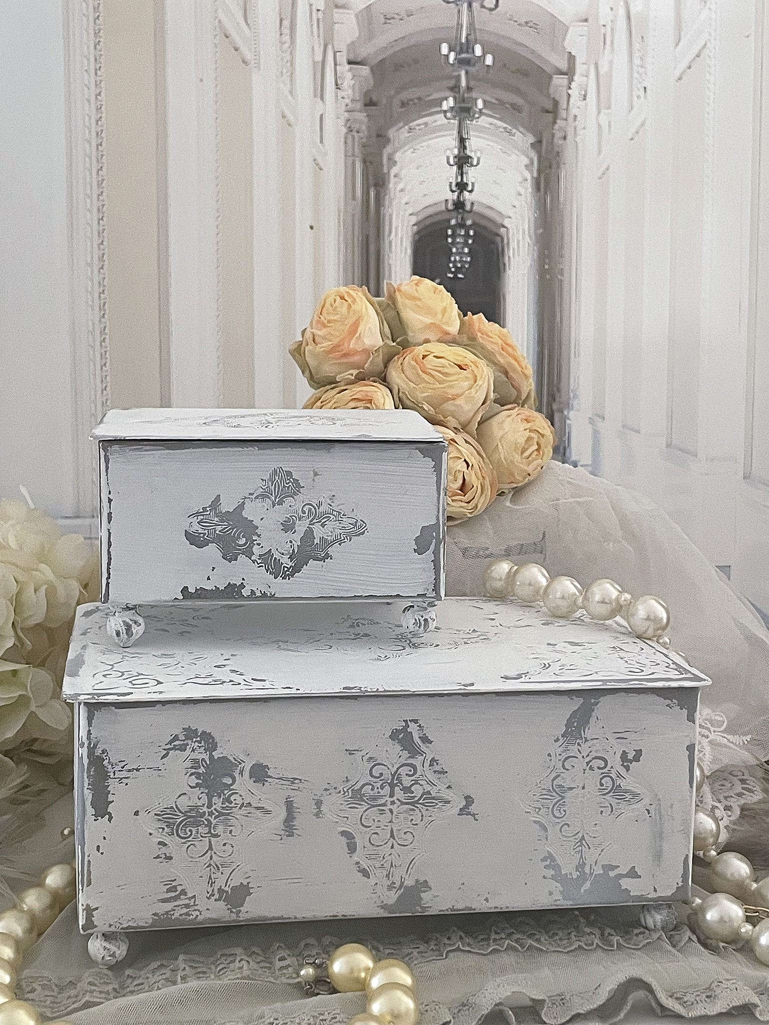 Zwei dekorative Aufbewahrungsboxen in hellblau mit Vintage-Muster, umgeben von Perlen und einer Rosenblüte.