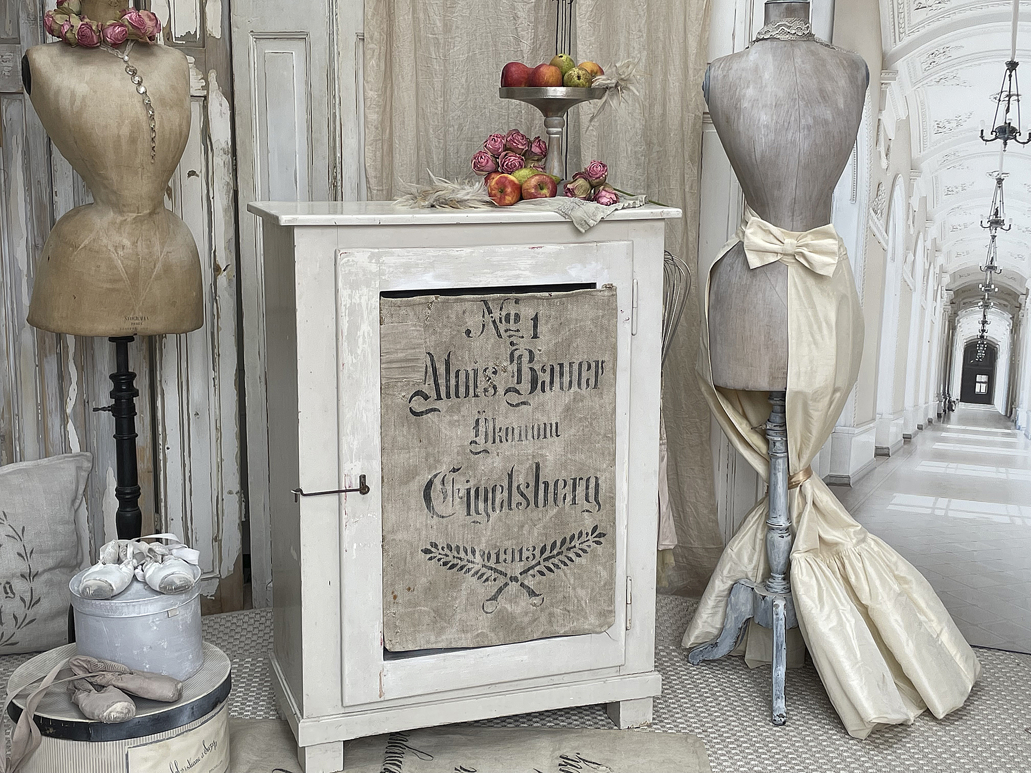 Vintage Dekorationsensemble mit Schneiderpuppen und Holzkasten Schneiderpuppen, ein Holzschrank und Obst auf einer silbernen Schale in stilvoller Dekoration