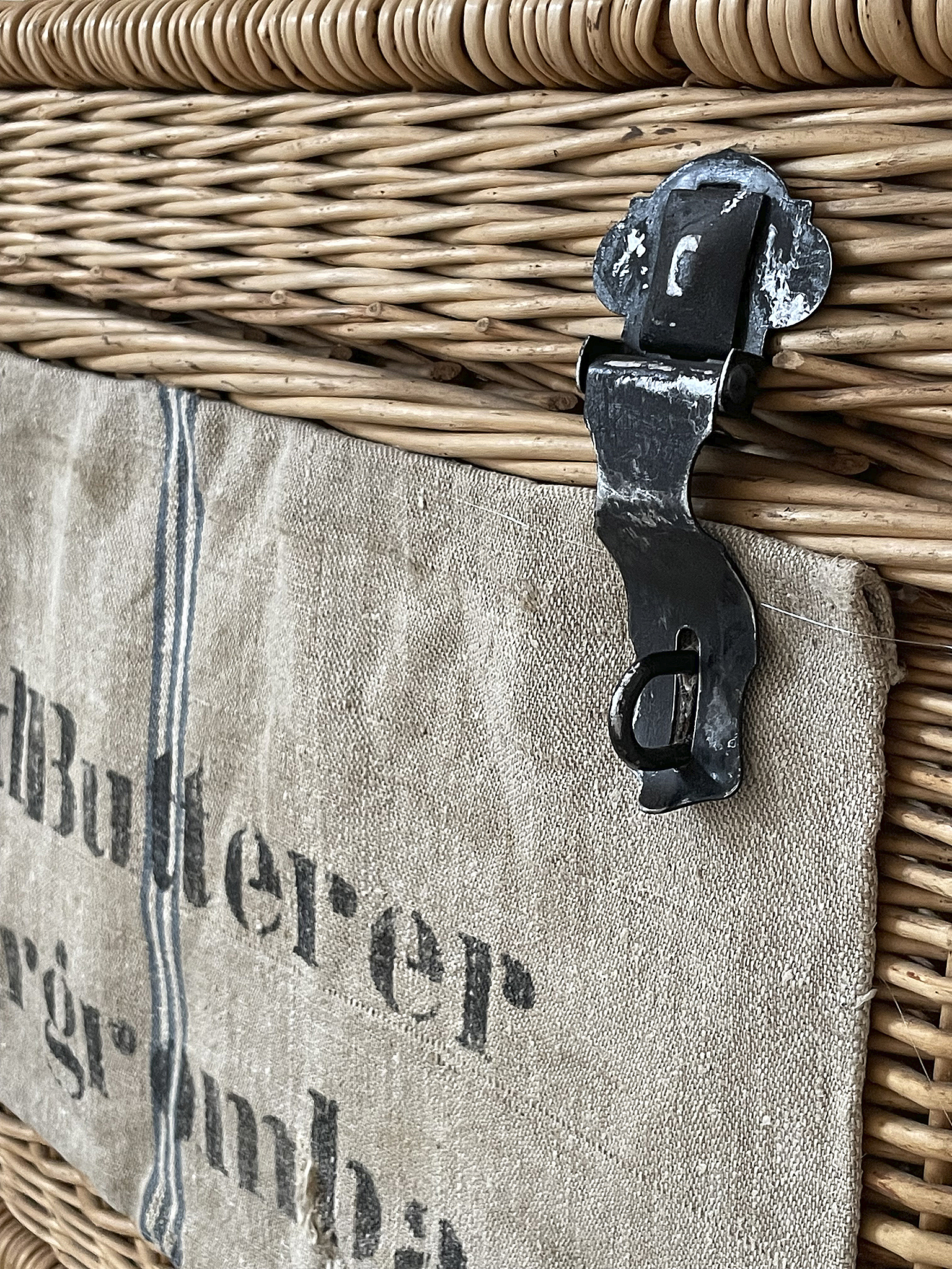 Handgefertigter Korb mit Metallschnalle und Leinwandbezug Detailaufnahme eines geflochtenen Korbs mit einer Metallschnalle und einem Leinwandbezug, der eine Beschriftung aufweist.