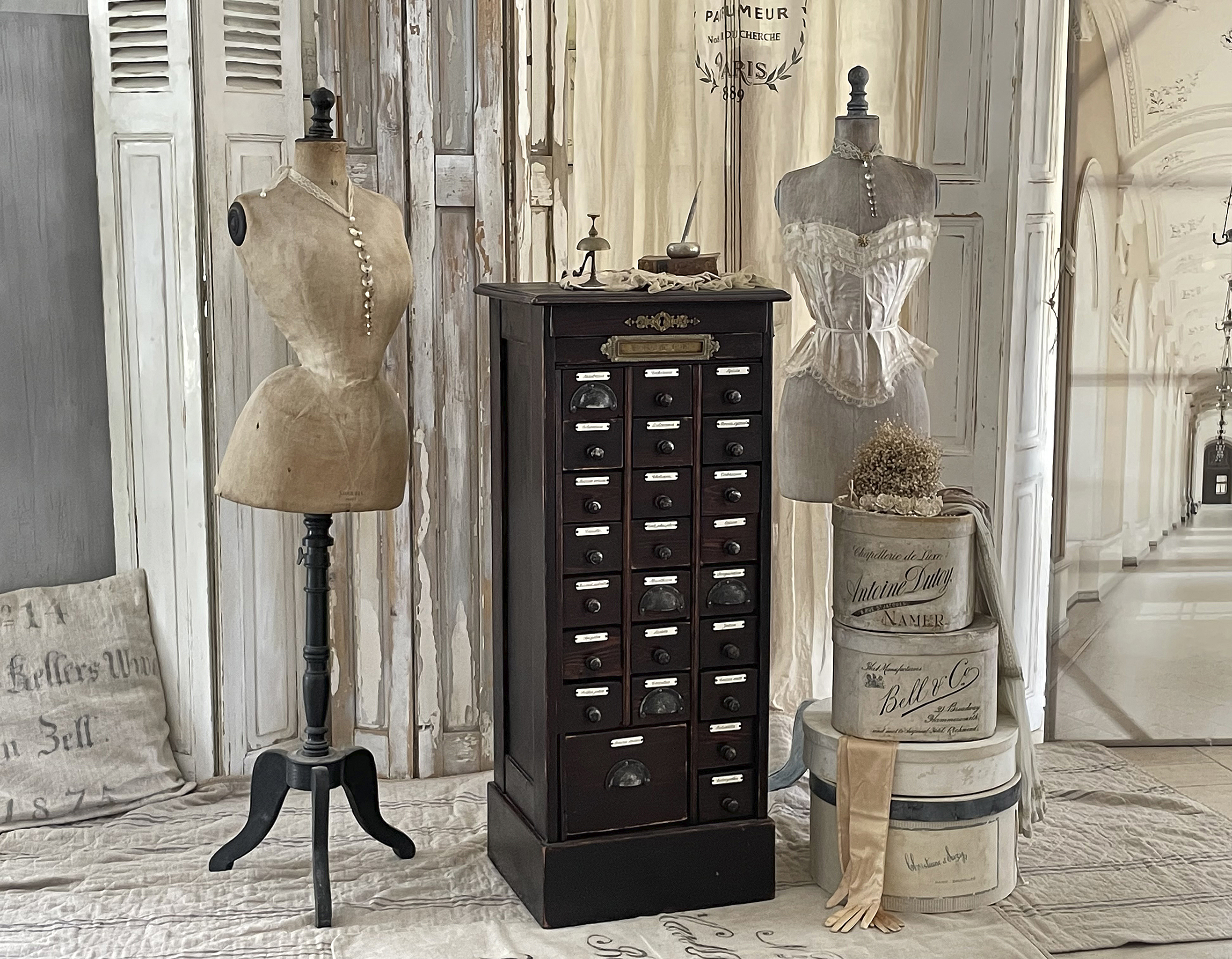 Ein Raum mit zwei Vintage-Mannequins und einer antiken Kommode voller Schubladen, umgeben von dekorativen Elementen.