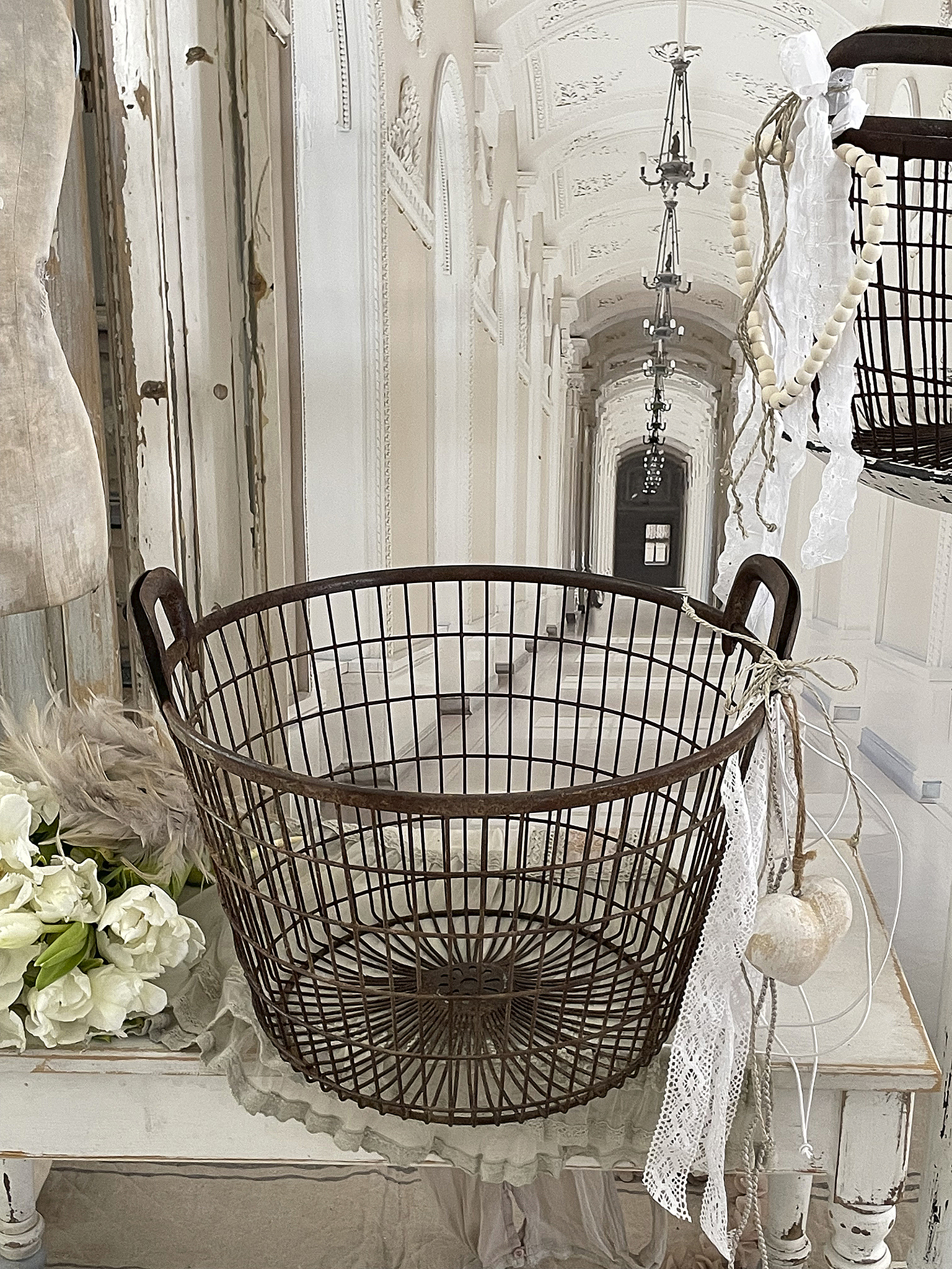 Dekorativer Drahtkorb im Vintage-Stil Eleganter Drahtkorb auf einem Holztisch, umgeben von Deko und Blumen im Hintergrund.