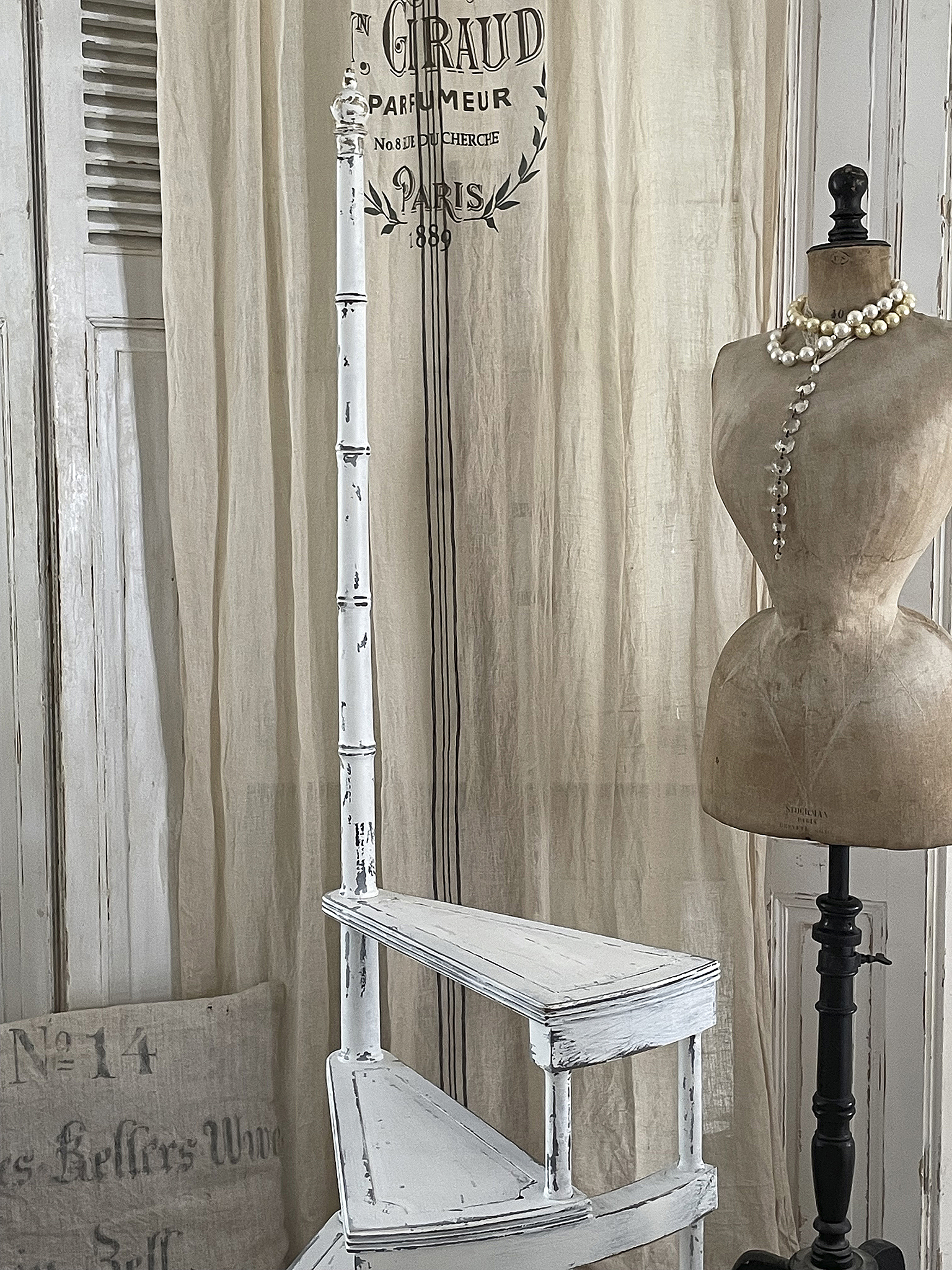 Vintage Treppenregal mit stilvollem Schneiderbüsten-Element Weißes, glattes Treppenregal und Schneiderpuppe vor einem dekorativen Vorhang.