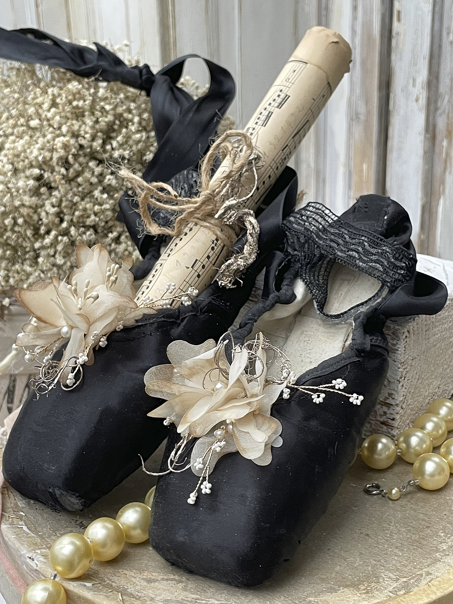 Dekorative schwarze Ballettschuhe mit Blumen und Notenrolle auf einem Tisch