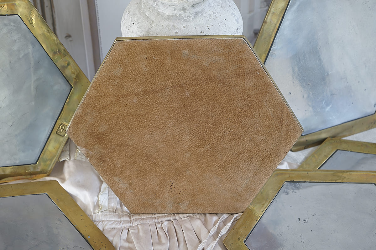 Detailansicht eines hexagonalen Spiegels mit goldfarbenem Rahmen und weichem, braunem Rückenteil
