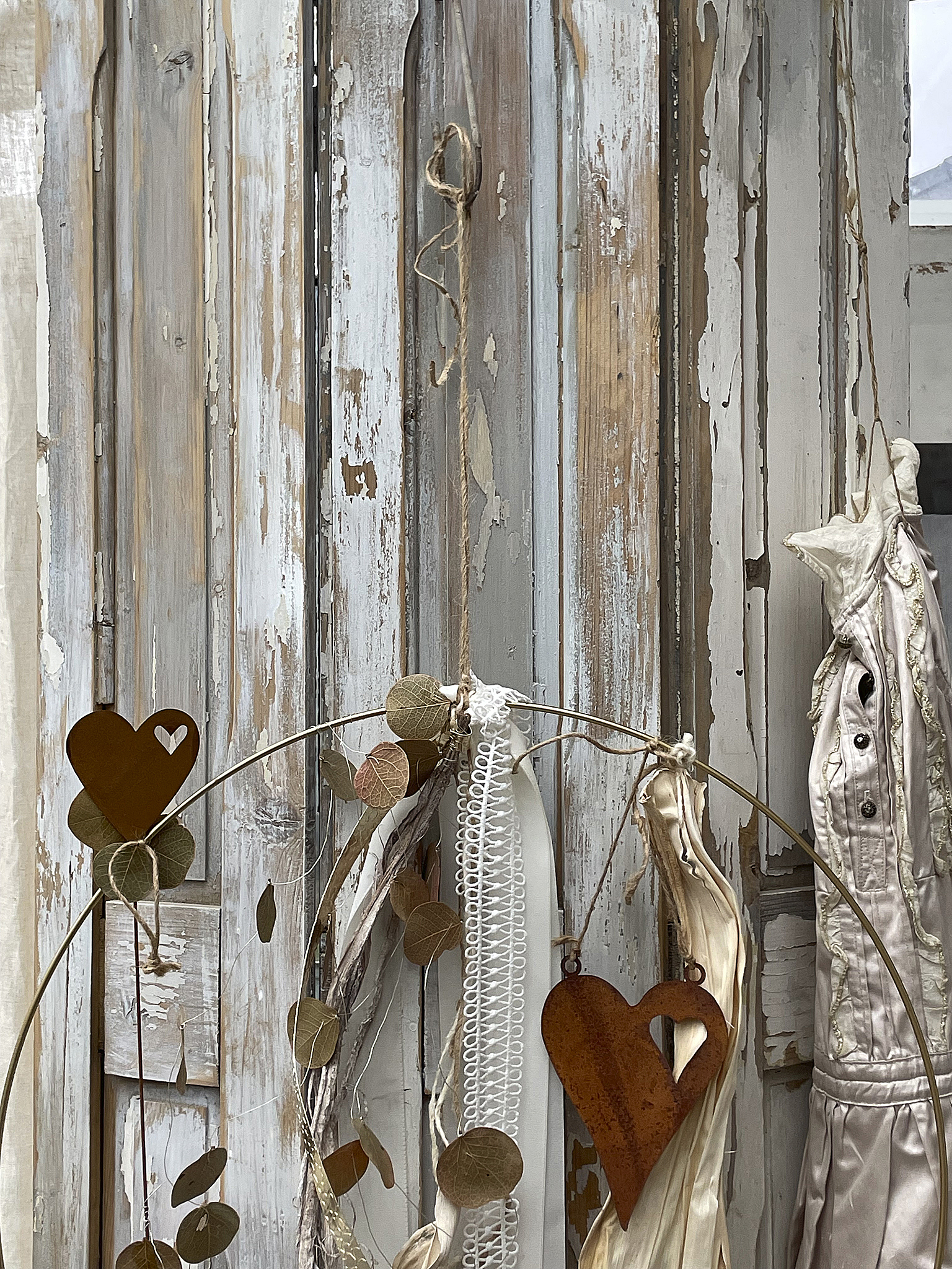 Dekorative Wandgestaltung mit Herzen und Naturmaterialien Dekoratives Element mit Herzen, Zweigen und vintage Stoffen an einer alten Holzwand
