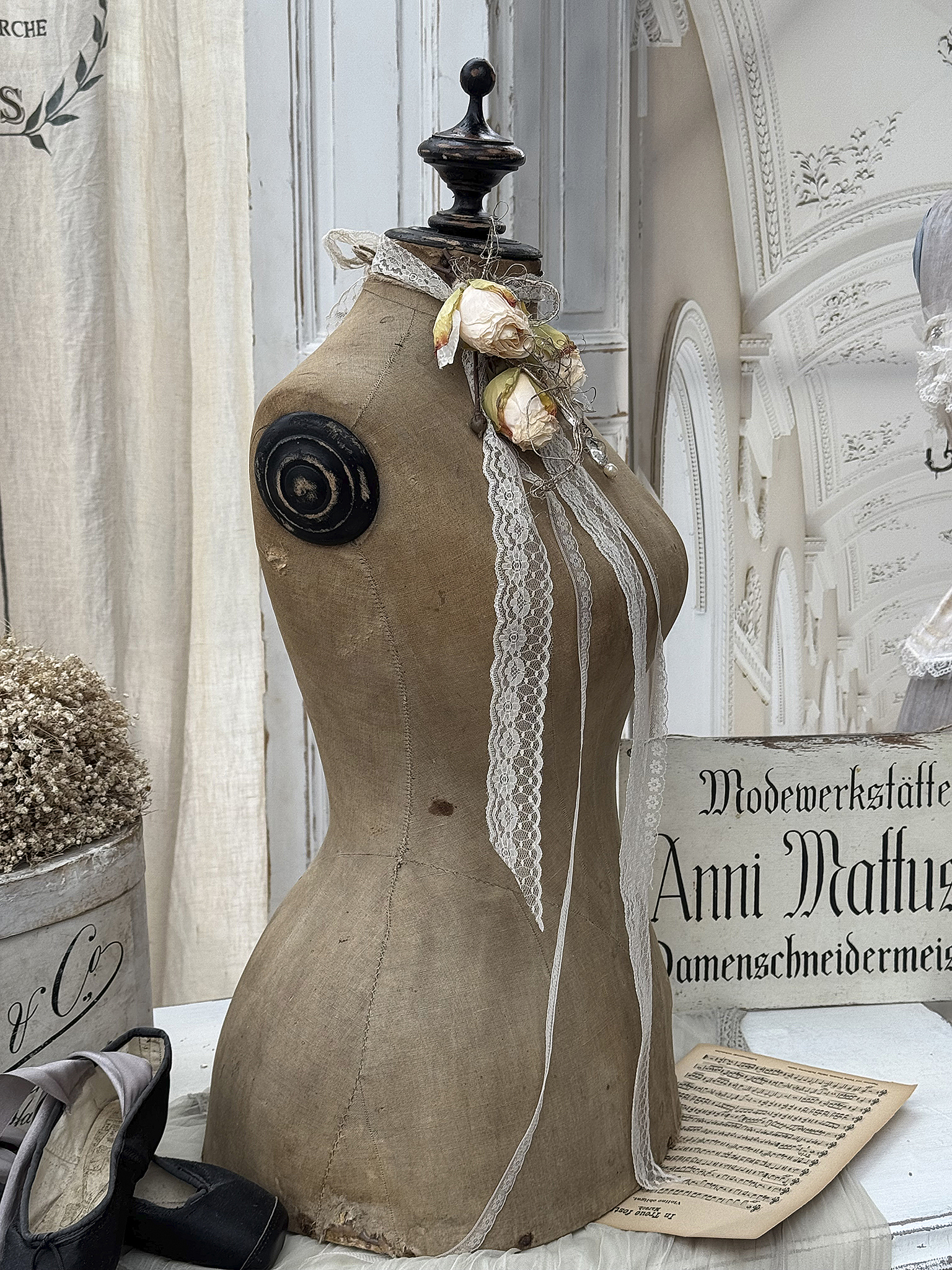 Deko-Schneiderpuppe mit Blumenverzierung und Rüschenband Ansicht einer dekorativen Schneiderpuppe mit Rüschenband und Rosendekoration, im Hintergrund eine stilvolle Inneneinrichtung.