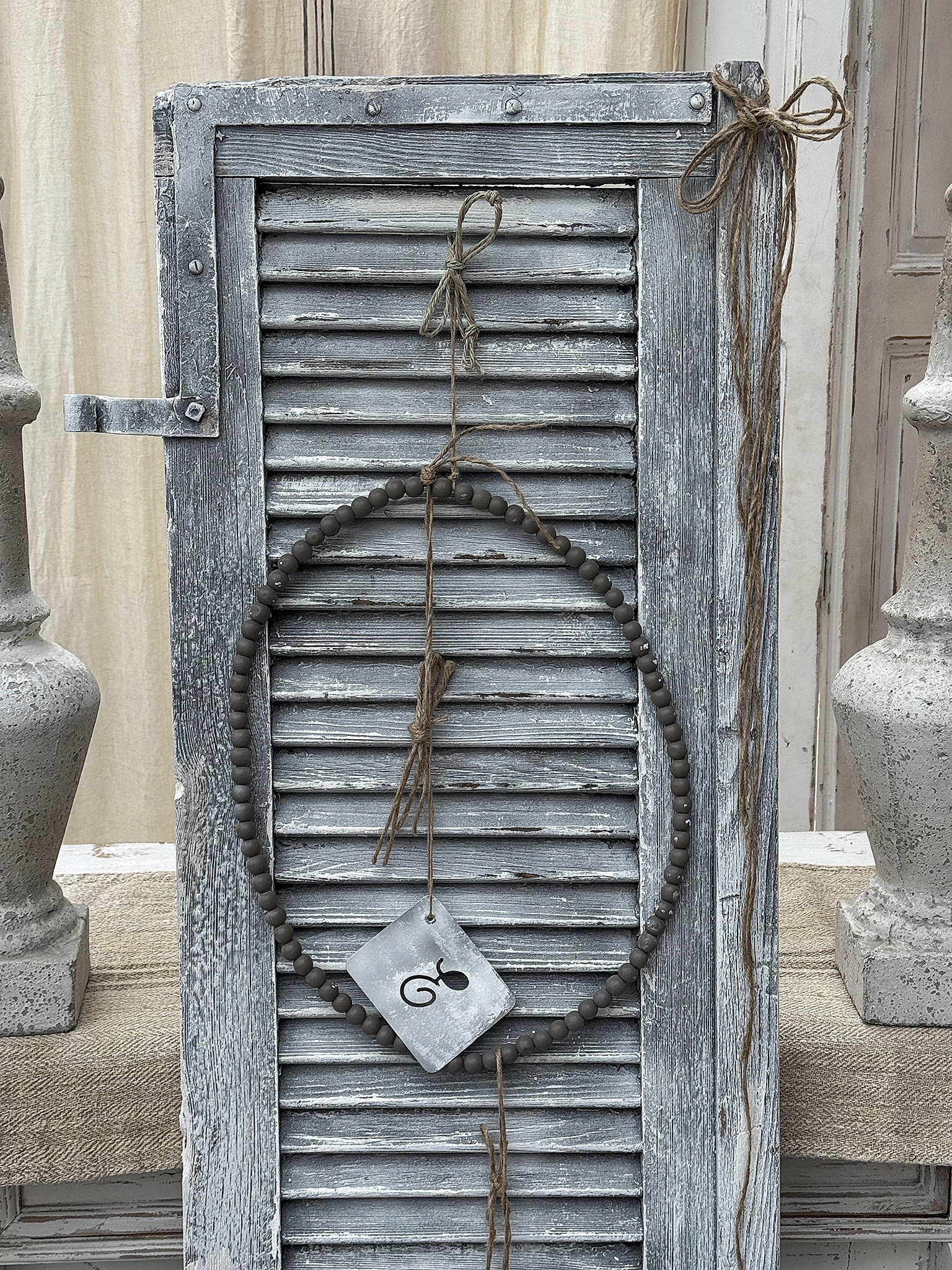 Dekorative Wandhängung mit Holzperlen und Schild Wanddeko aus Holzperlen und einem Schild an einer alten Fensterlade