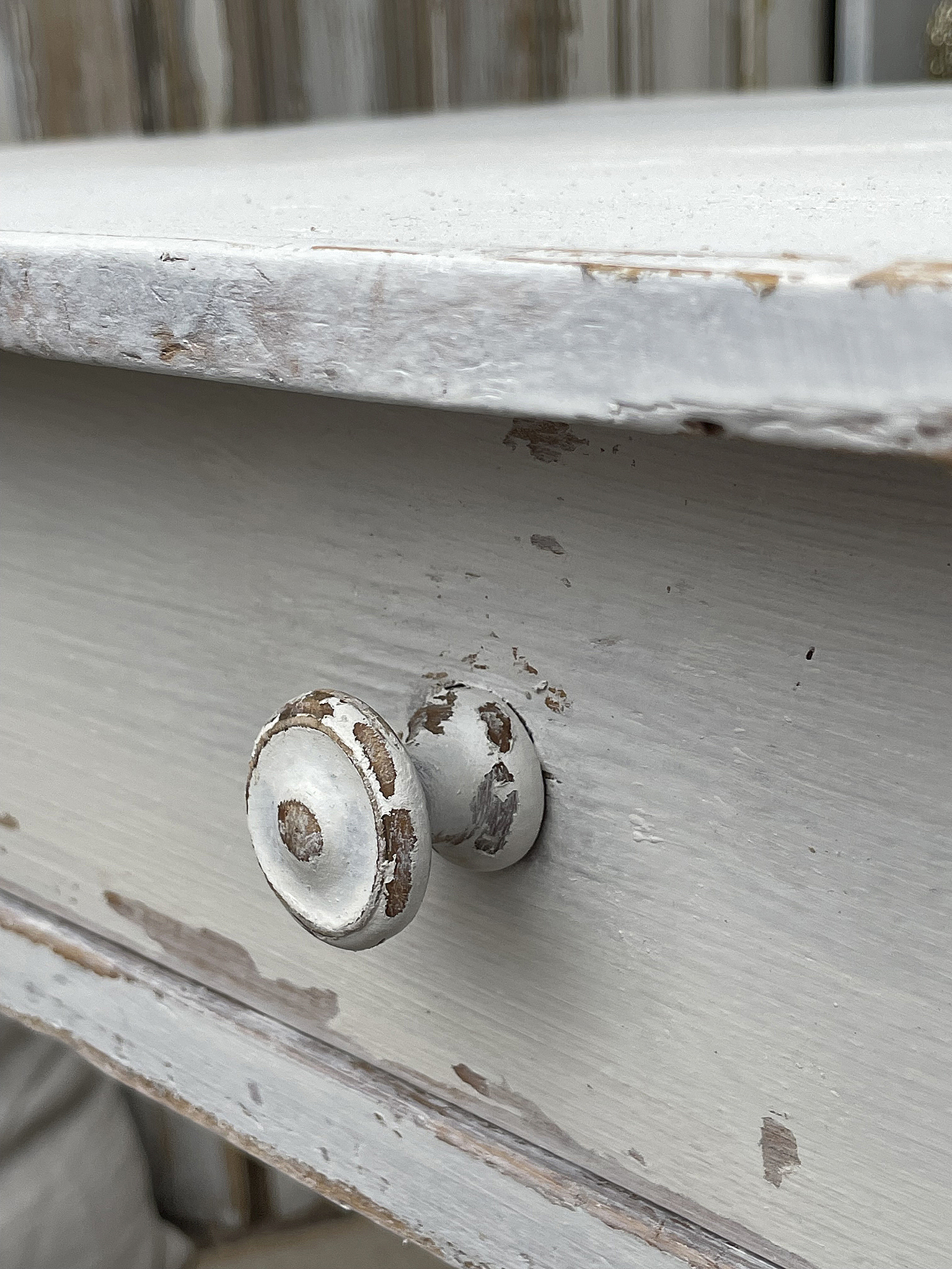 Detailaufnahme eines weißen Möbelknaufs mit ausgewählter Patina Nahaufnahme eines abgenutzten weißen Möbelknaufs an einem Tisch