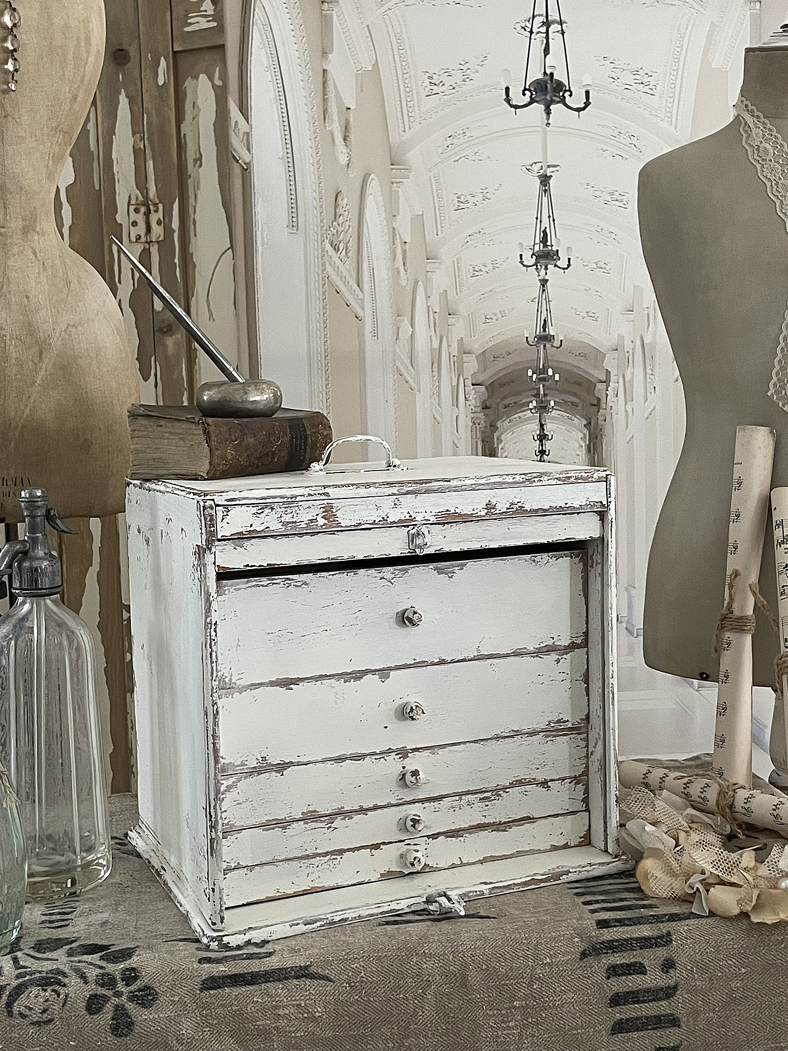 Decorative vintage storage box with distressed white finish, featuring five drawers and placed in a stylish interior setting.
