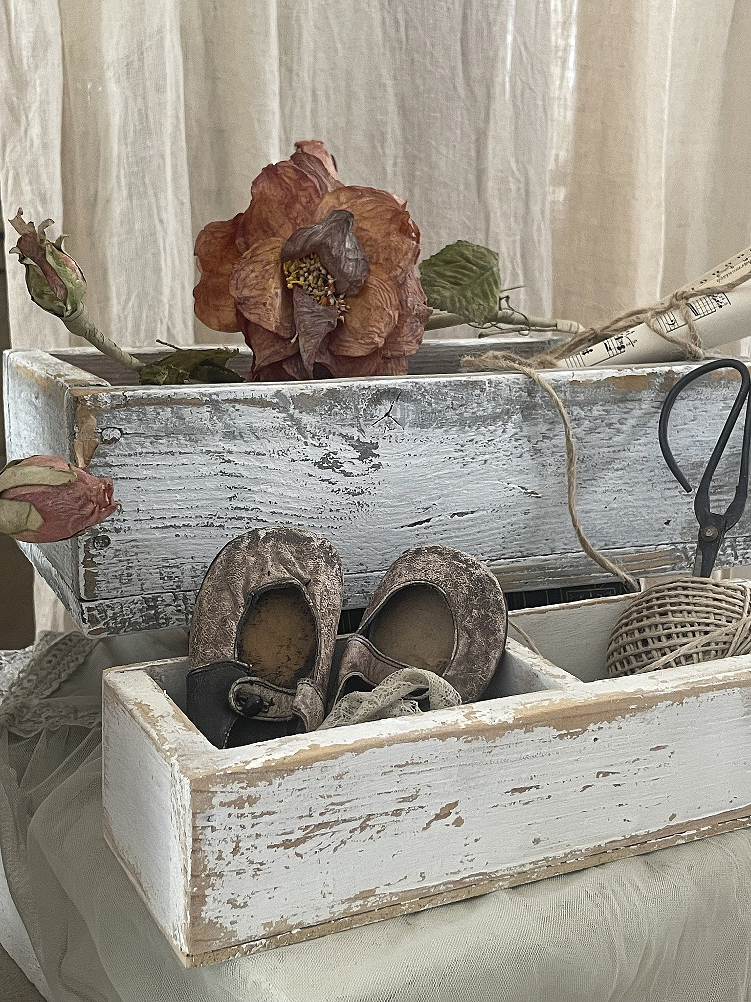 Vintage Kinderschuhe und Deko-Elemente in einer rustikalen Holzbox Rostige Kinderschuhe und eine vergängliche Blume in einer Holzbox auf einem Tisch