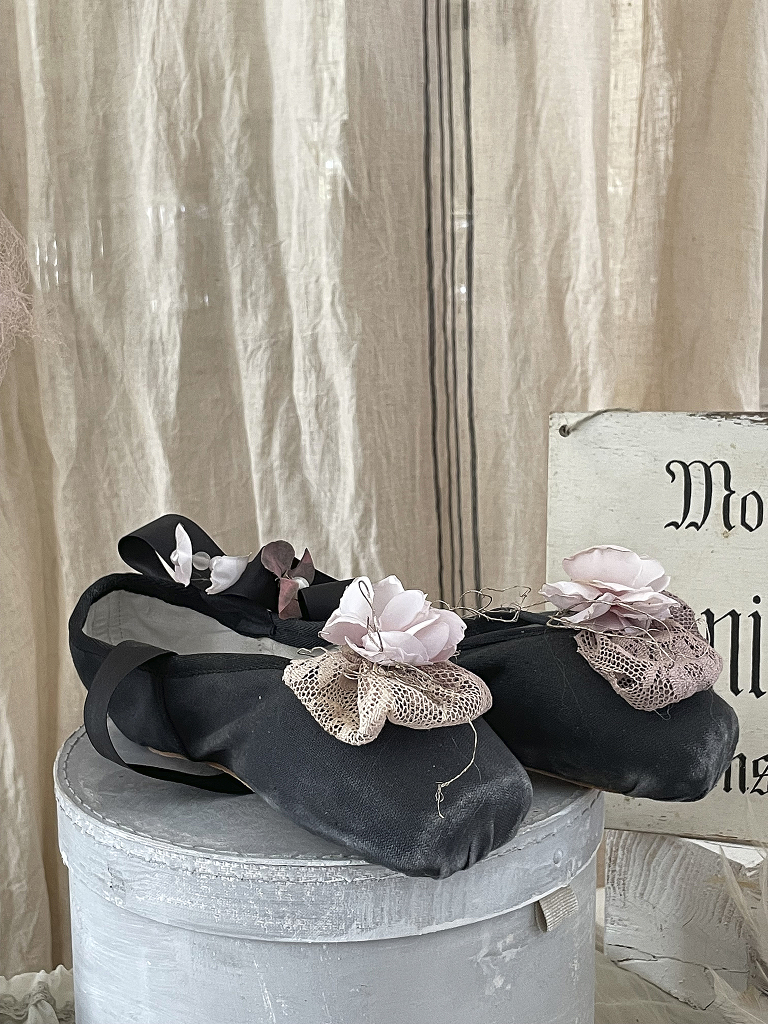 Schicke schwarze Ballettschuhe mit Blumenapplikationen Schwarze Ballettschuhe dekoriert mit rosa Blumen auf einem hölzernen Untergrund