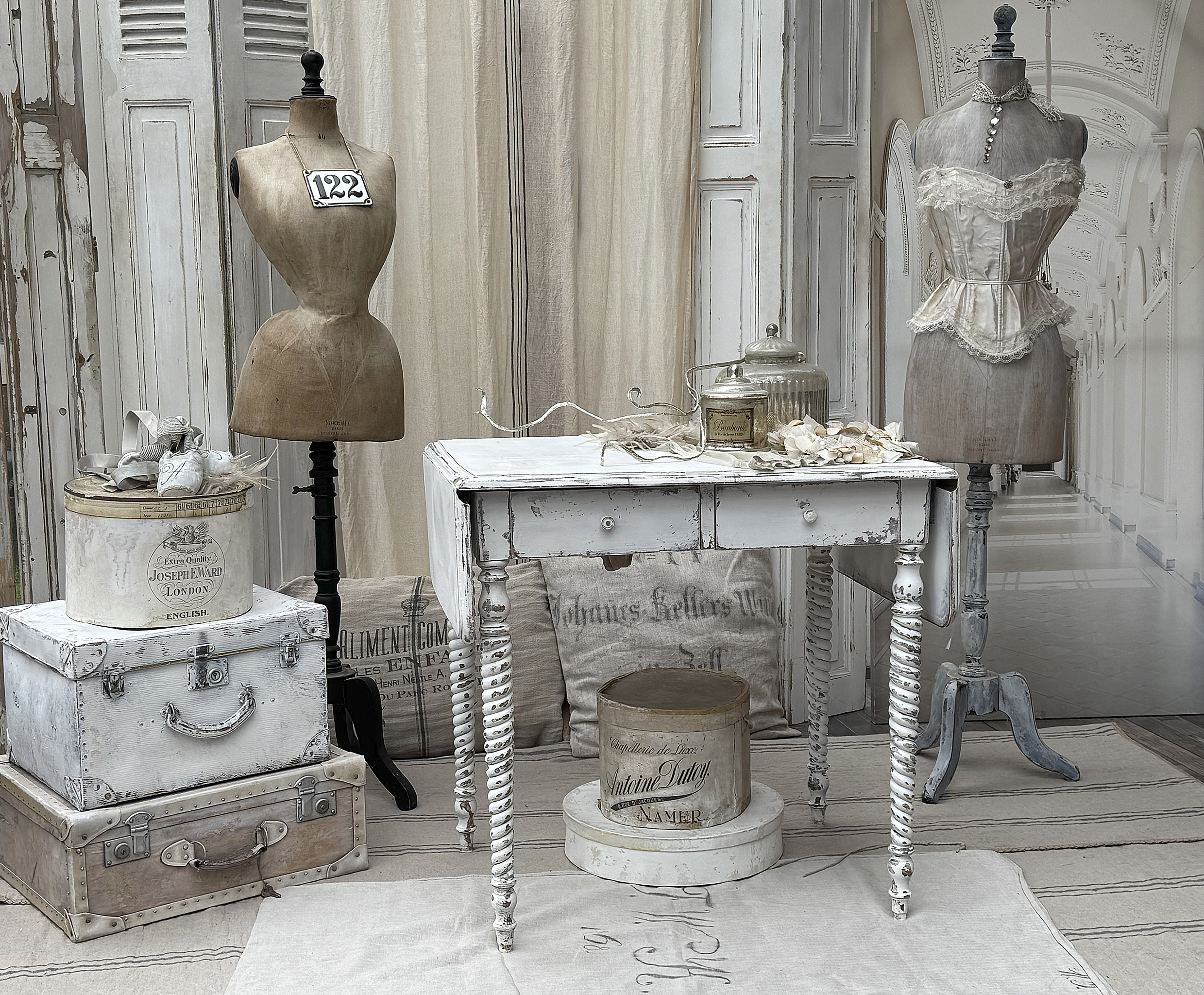 Rustikales Interieur mit zwei Mannequins, einem weißen Tisch und antiken Koffern