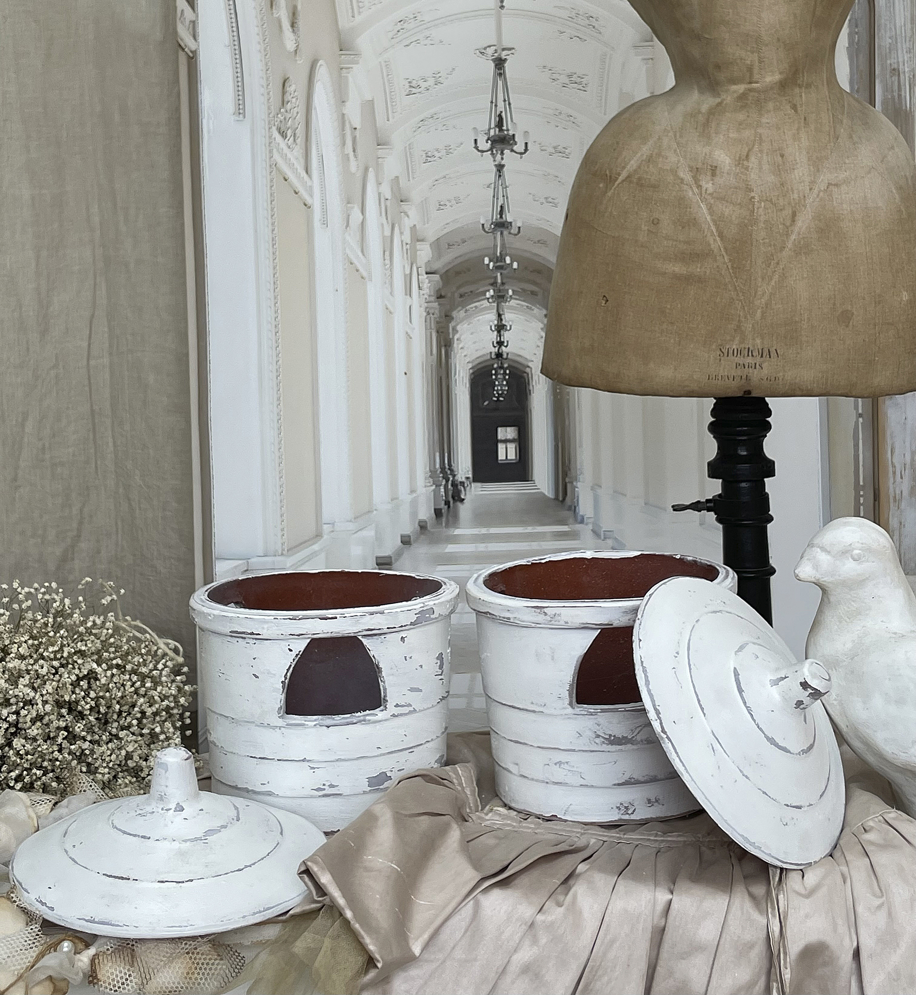 Dekorative Aufbewahrungstöpfe in Vintage-Optik Zwei weiße Vintage-Aufbewahrungstöpfe mit Deckeln, eine Schneiderpuppe und eine Keramikfigur in einem eleganten Raum