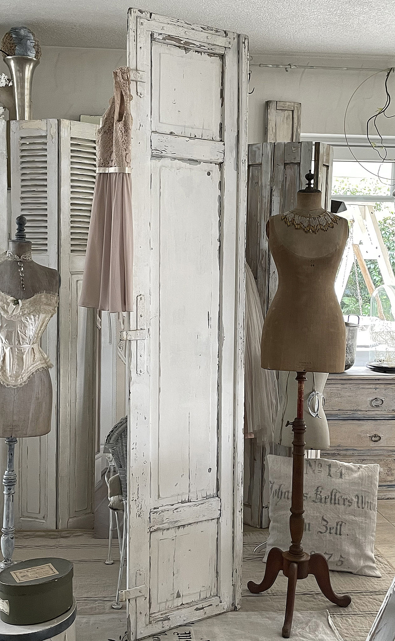 Einblicke in einen stilvollen Raum mit einer alten weißen Tür, Schaufensterpuppen und einem eleganten Kleid