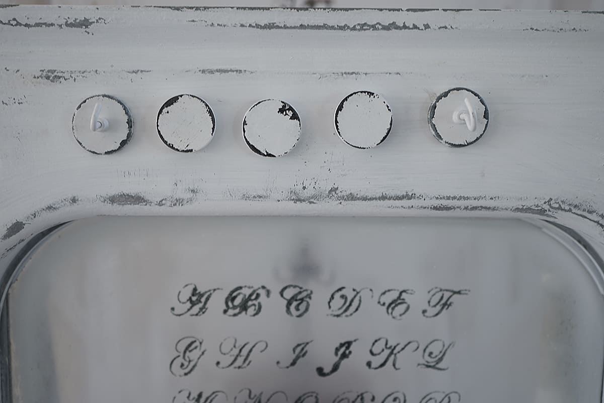 Detailansicht eines Vintage-Elements mit Buchstaben und weißen Knöpfen auf einer grauen Oberfläche