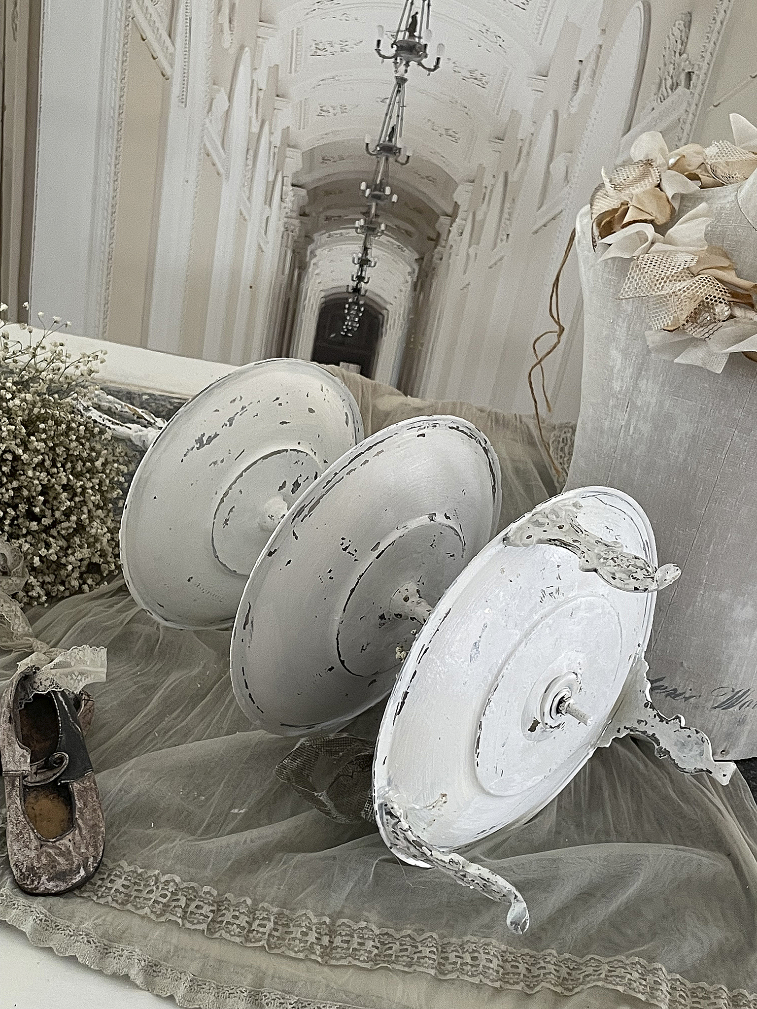 Dekorative weiße Kerzenhalter auf einem nostalgischen Untergrund Drei weiße Kerzenhalter aus Metall auf einem zarten Tischtuch mit Vintage-Elementen.