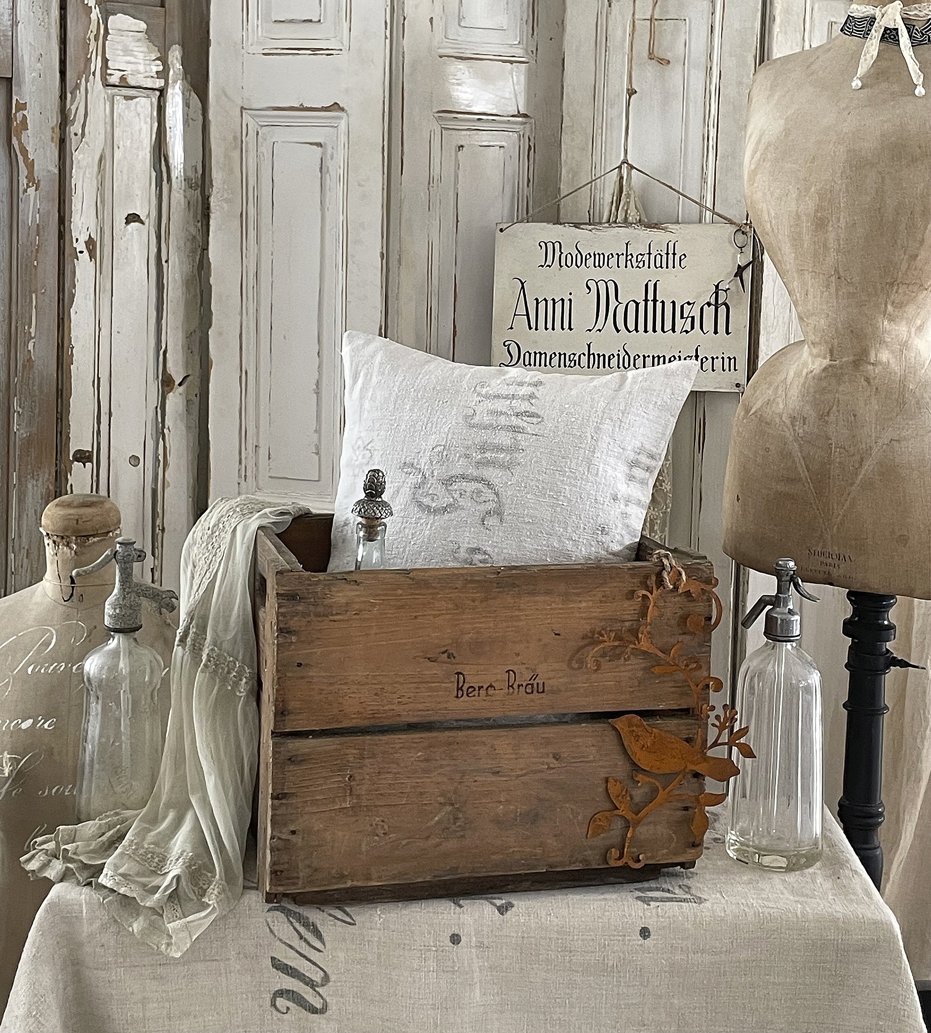 Rustikales Holzgestell mit weißen Kissen und vintage Dekoration Holzbox mit Kissen, antiken Flaschen und Schneiderpuppe auf einem Tisch