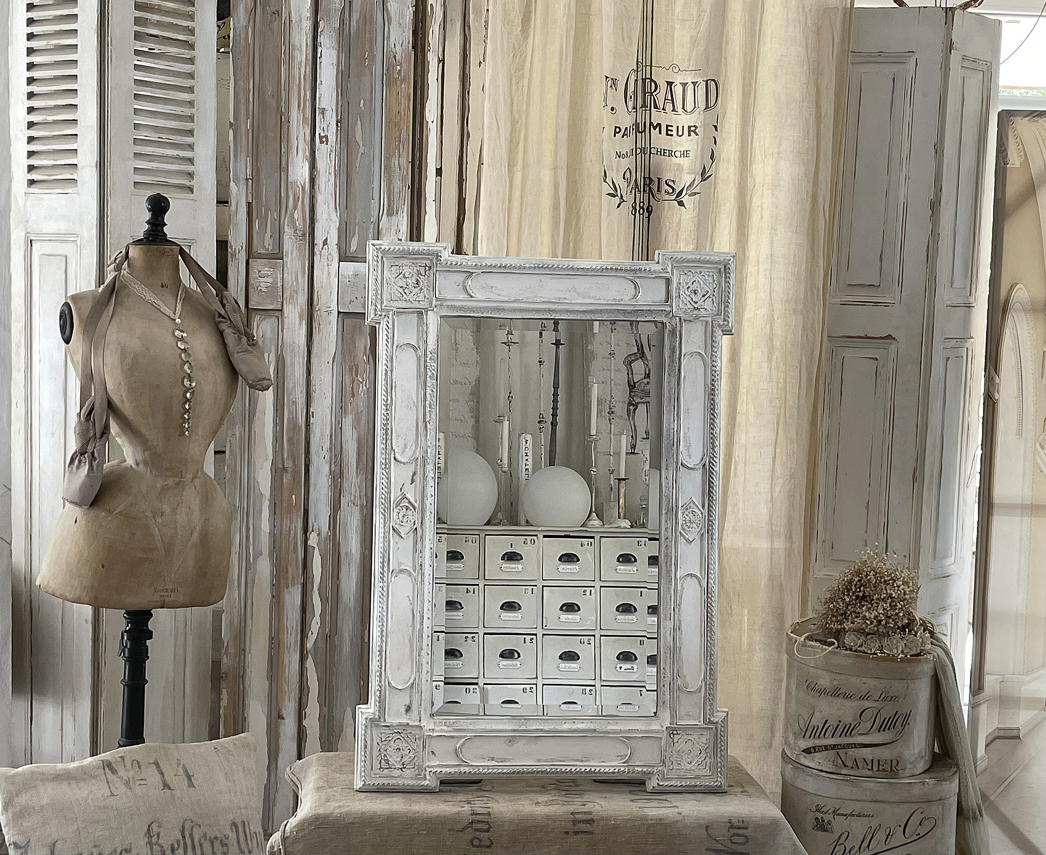 Eleganter Spiegel im Vintage-Stil mit dekorativen Elementen Antiker Spiegel mit kunstvollem Rahmen, daneben eine Schneiderpuppen und Holzregale im minimalistischen Raum.