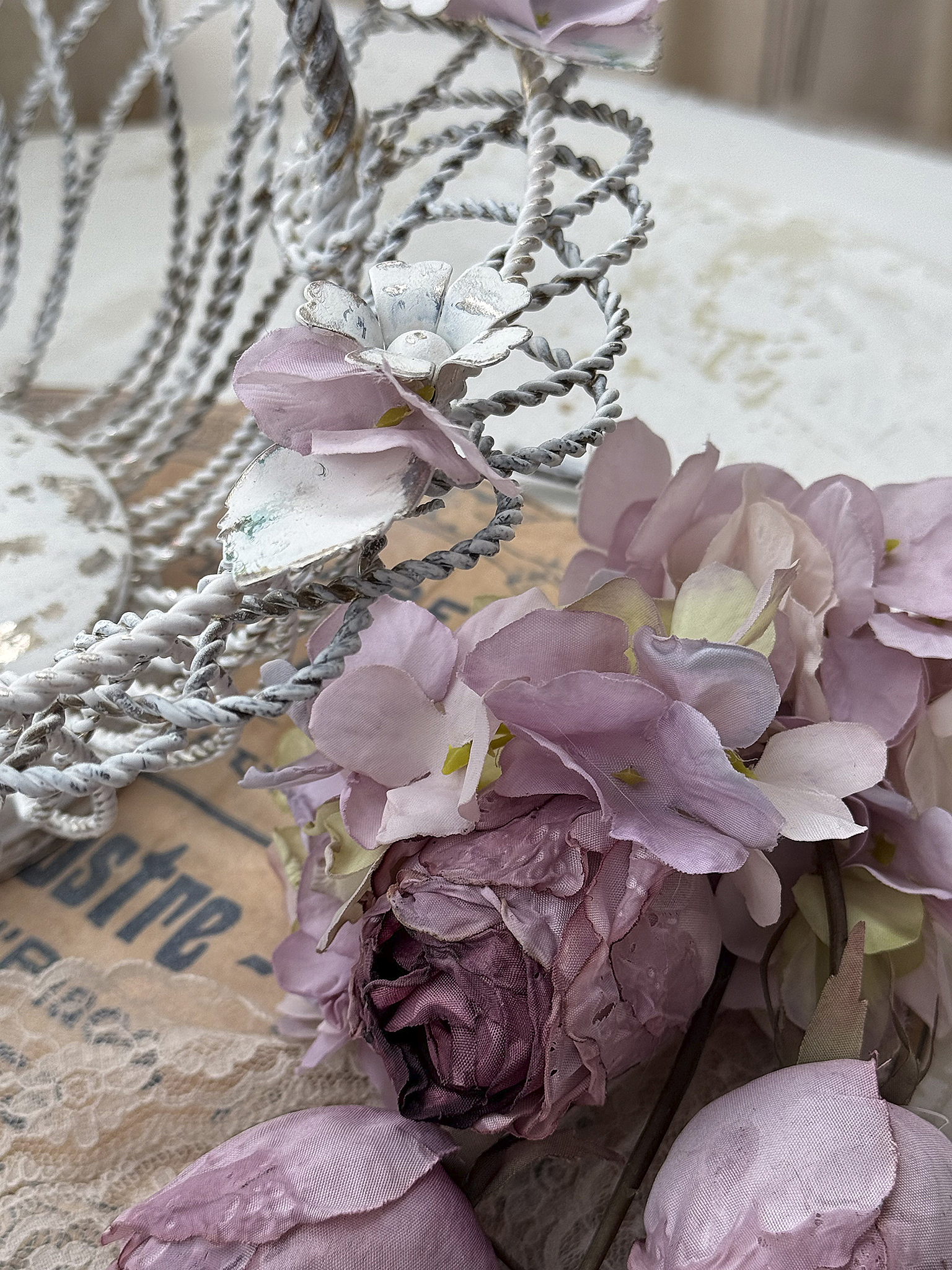 Dekorative Blumenarrangement mit zarten, rosa Seidenblumen und Metallkorb Nahaufnahme eines zarten Dekorationsarrangements mit rosa Seidenblumen und einem dekorativen Metallkorb auf einem vintage Hintergrund