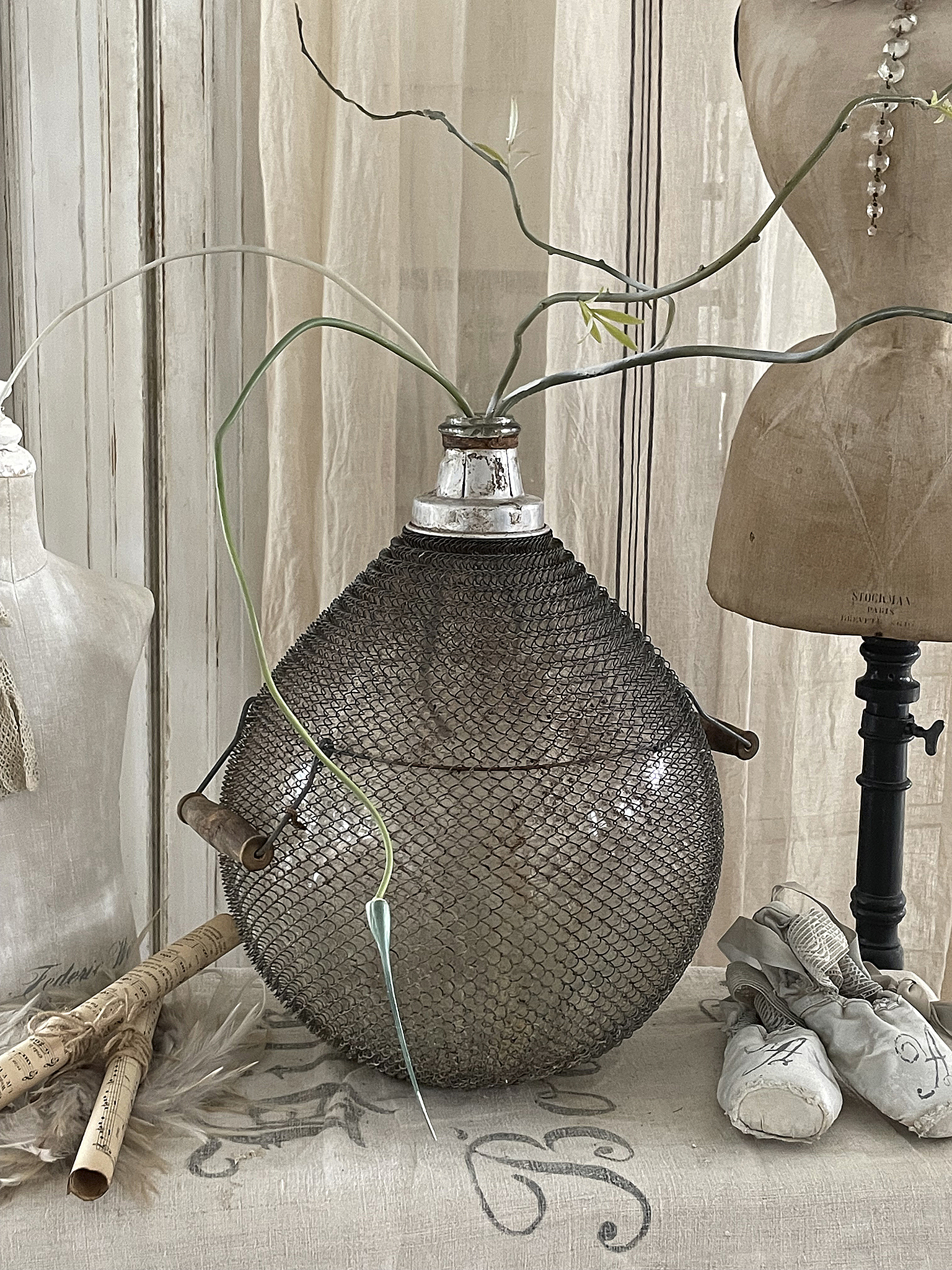 Elegante Vintage-Vase mit Pflanzen, stilvolle Inneneinrichtung Vintage-Vase aus Draht mit Pflanzen, umgeben von Dekorationsobjekten in einem stilvollen Raum
