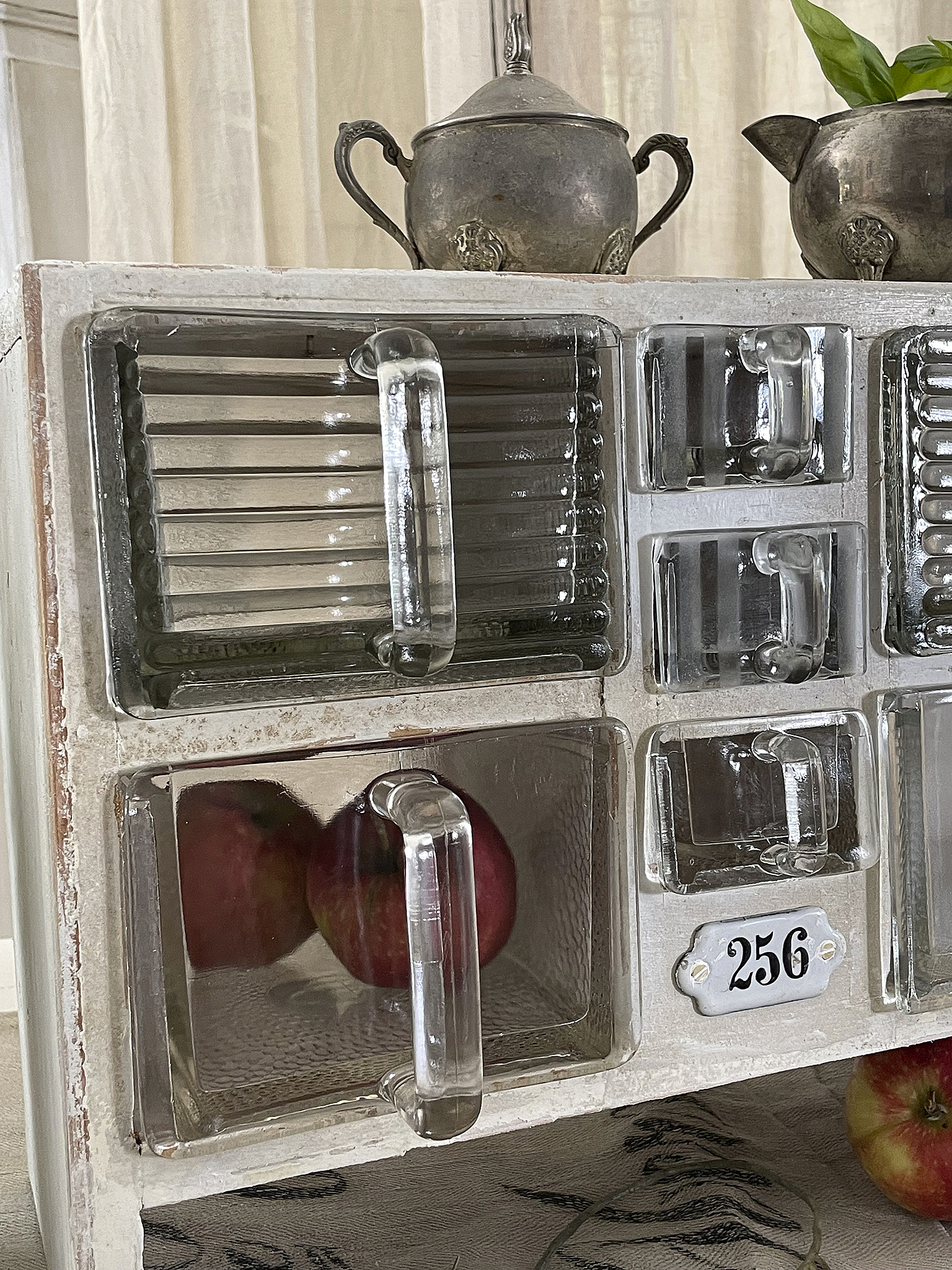 Vintage Glasvitrine mit Äpfeln und Silbergeschirr Detailansicht einer Glasvitrine mit Äpfeln und Vintage-Silbergeschirr