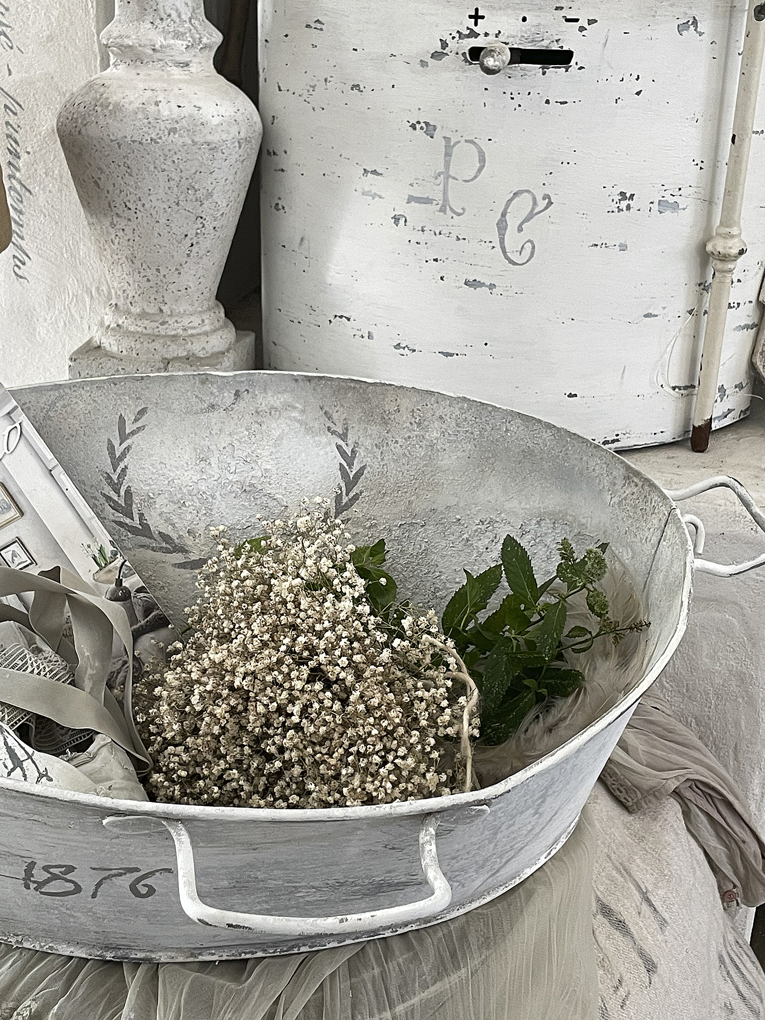 Dekorativer Eimer mit Trockenblumen und Stoffen Stilvolle Deko in einem Eimer mit Trockenblumen, umgeben von verschiedenen Textilien und Accessoires