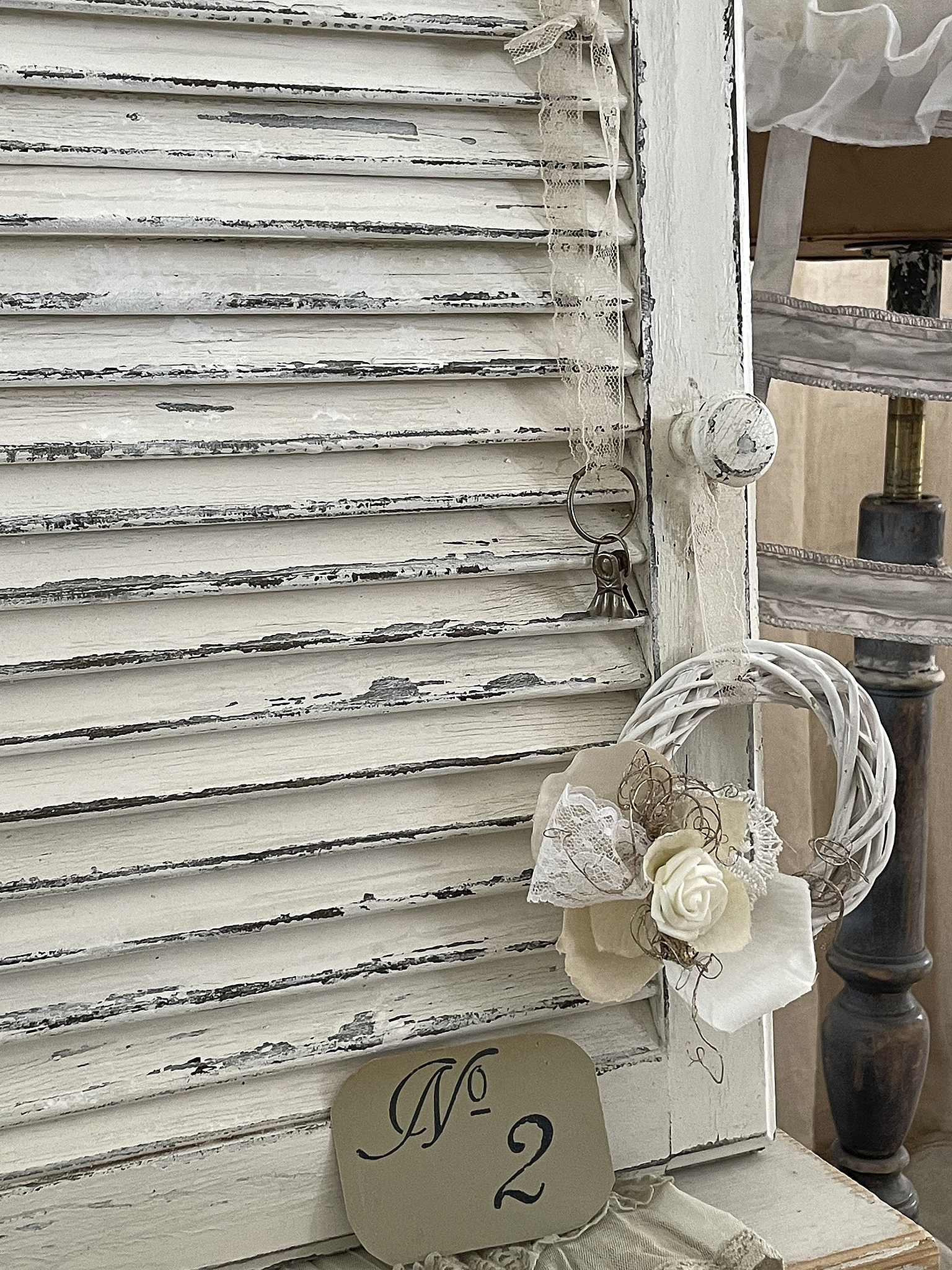 Dekorativer Shabby-Chic Fensterladen mit Schlüssel und floralem Kranz Shabby-Chic Fensterladen in Weiß mit Schlüsselanhänger und blumigem Kranz, Nummer 2